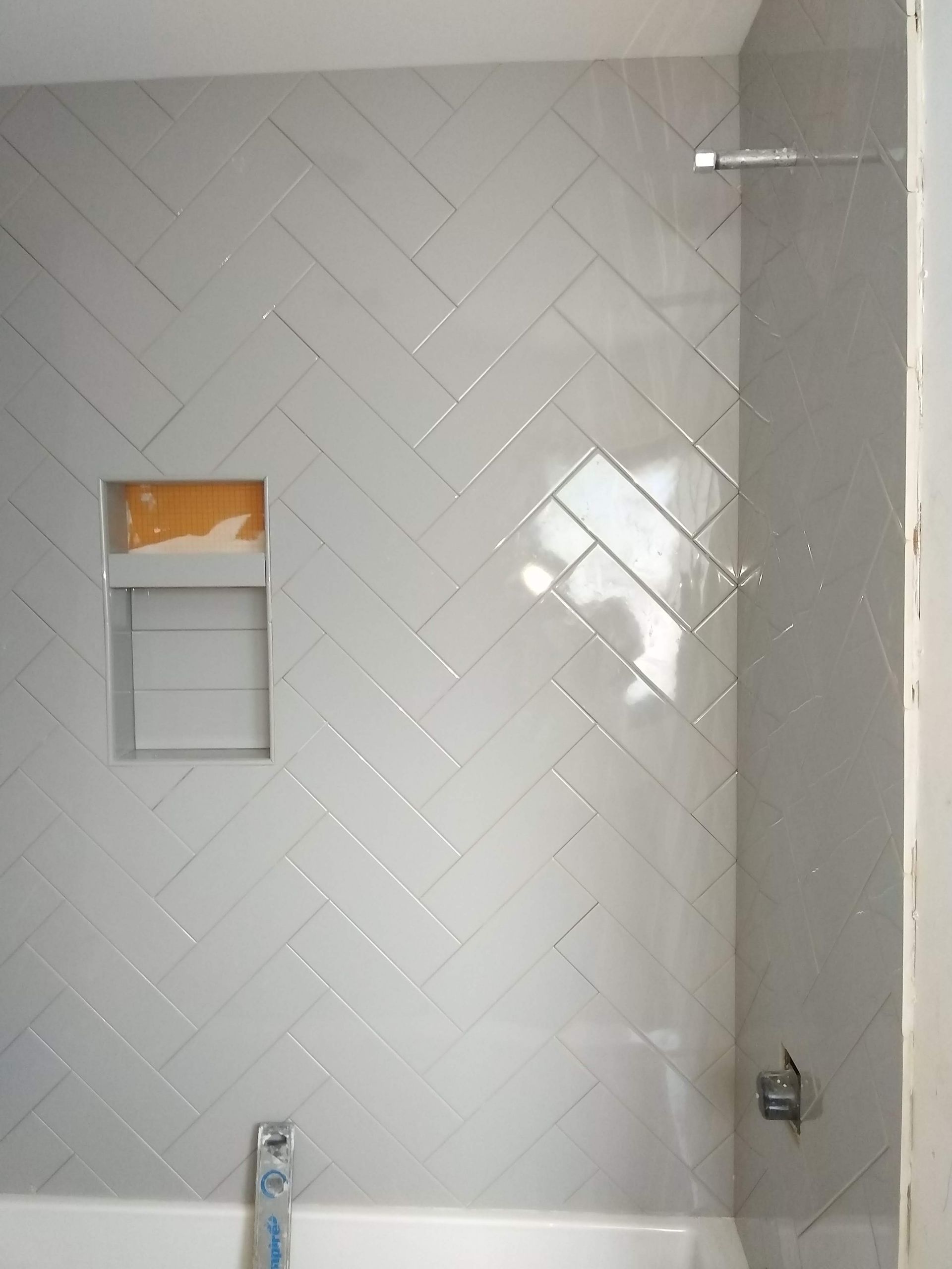 Partially tiled bathroom wall with a shower niche and chrome fixtures
