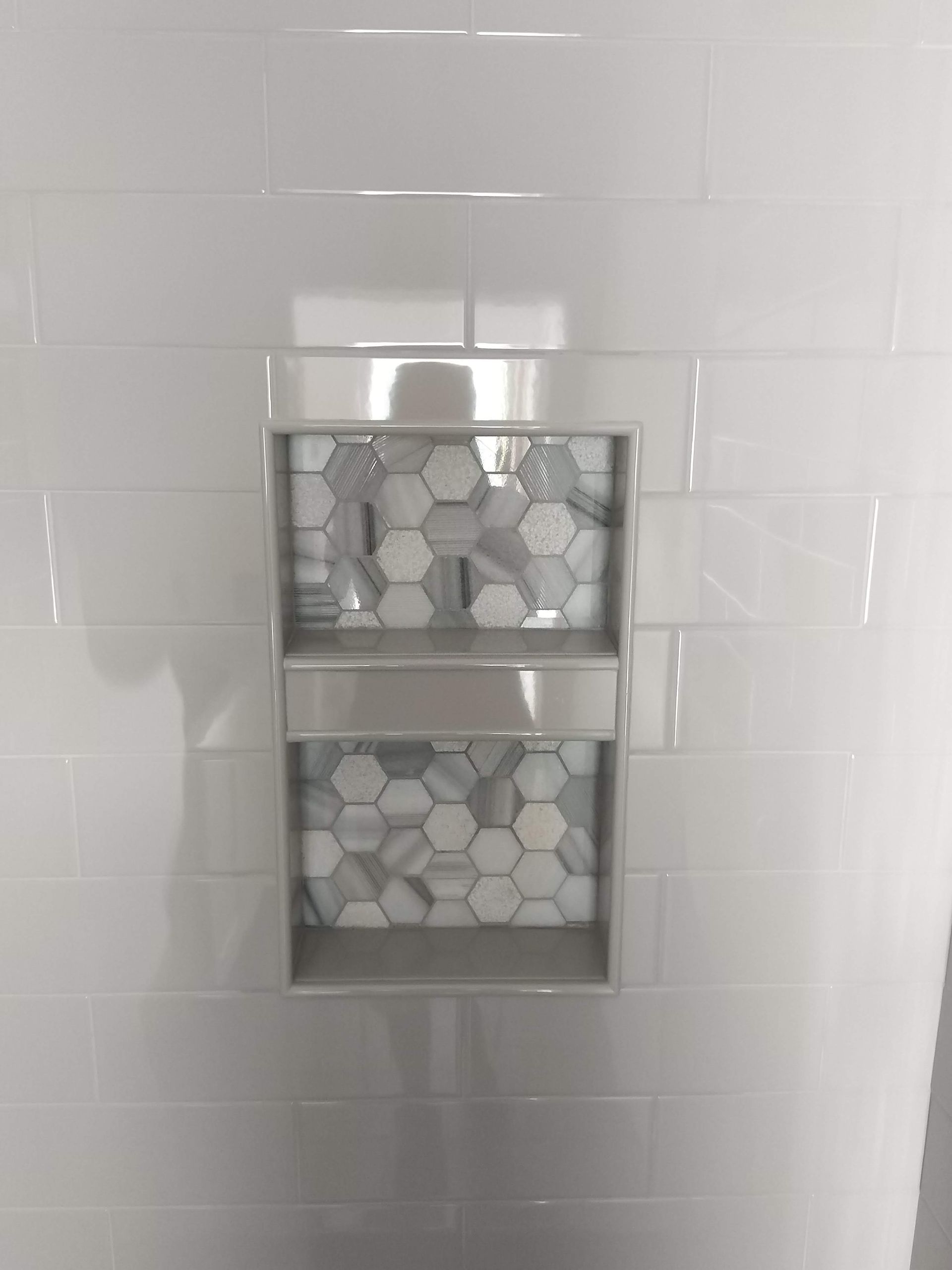 Chrome bathroom shelf with hexagon-tiled items mounted on a white tiled wall