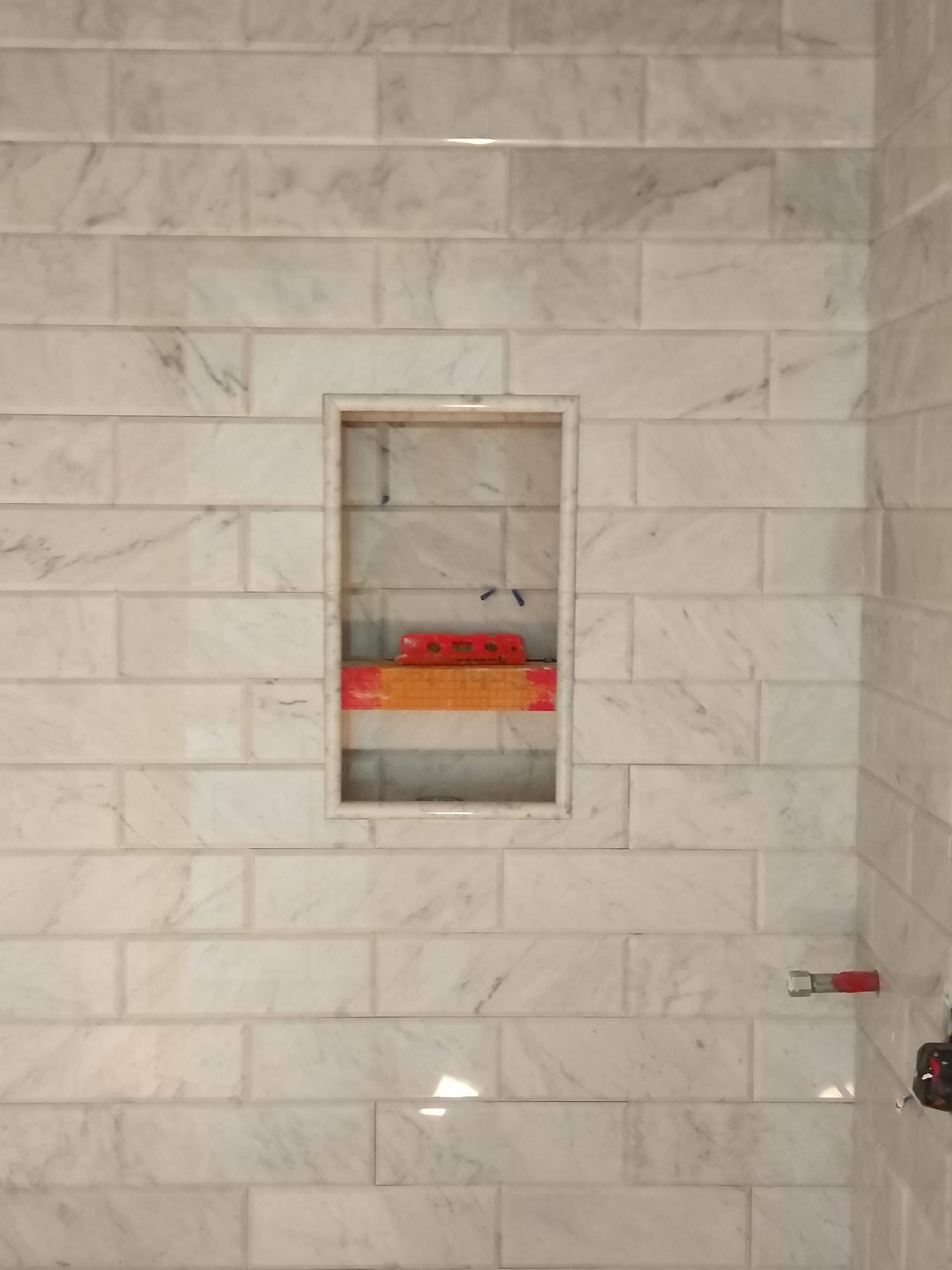 Tiled wall with a small recessed niche holding orange items and red containers