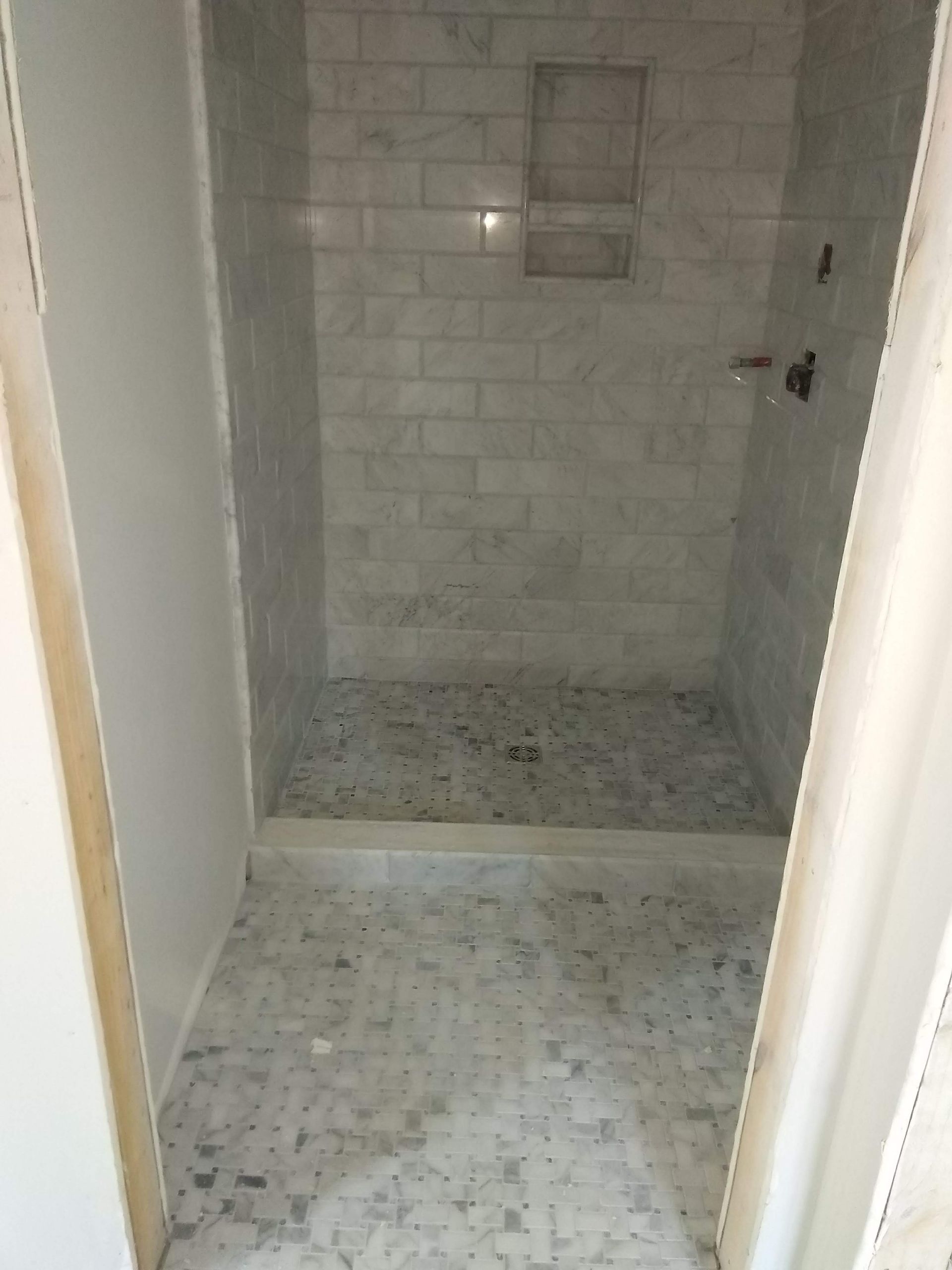Empty tiled shower stall with a shower niche and built-in bench, viewed through a doorway.
