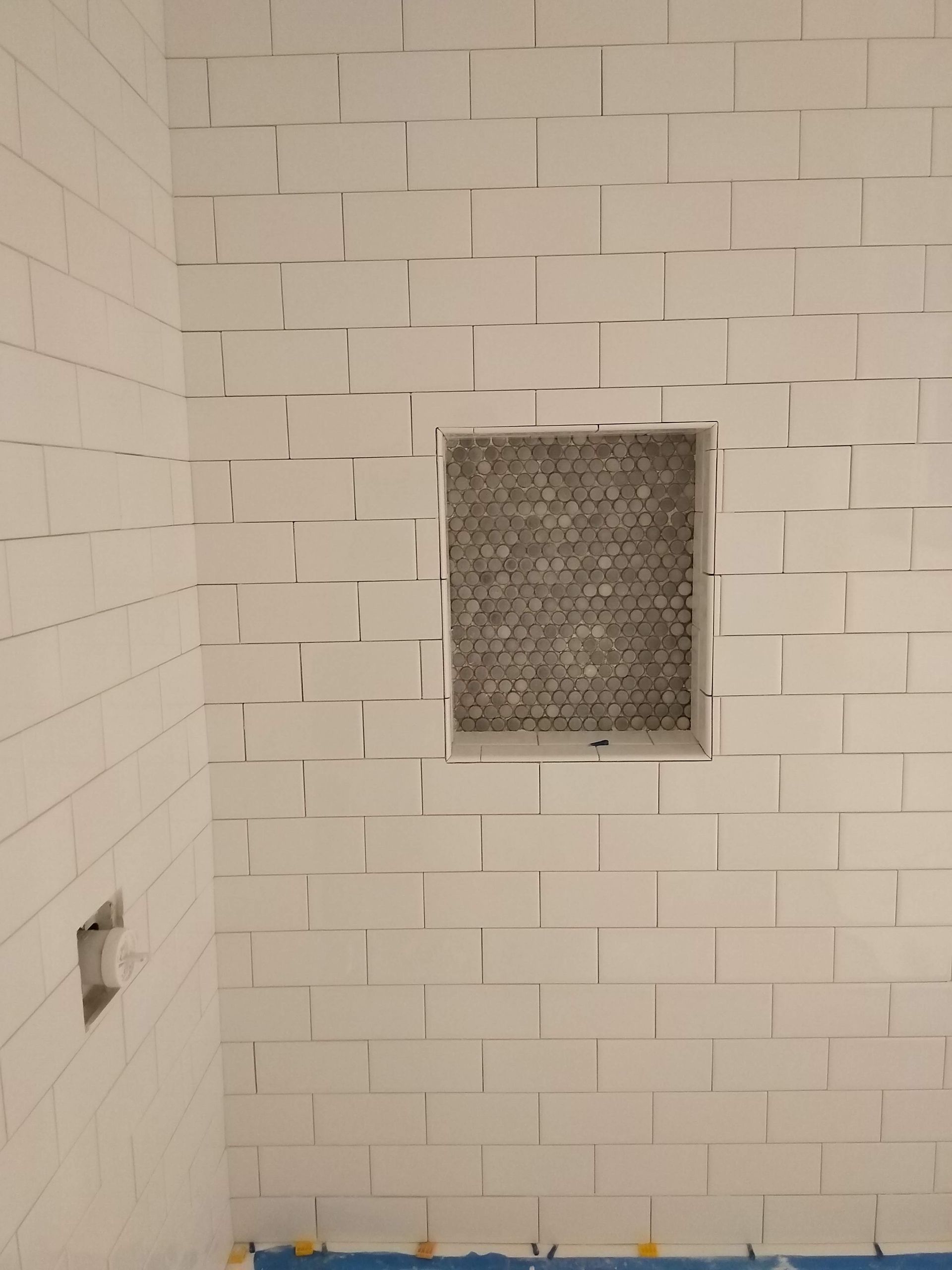 White tiled shower wall with a square frosted glass window and blue tape at the bottom