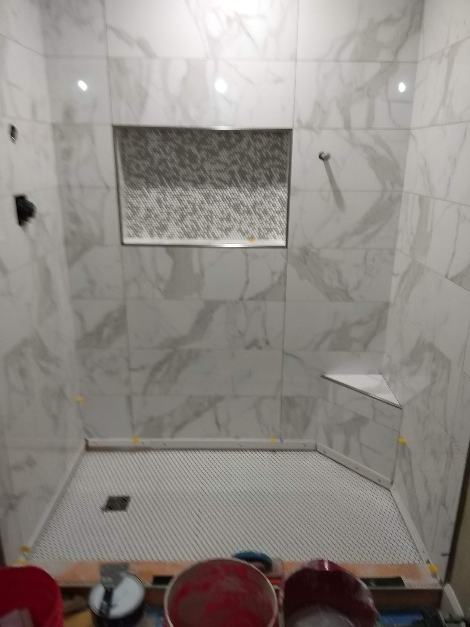 White tiled walk-in shower with built-in shelf, bench, and a small floor drain.