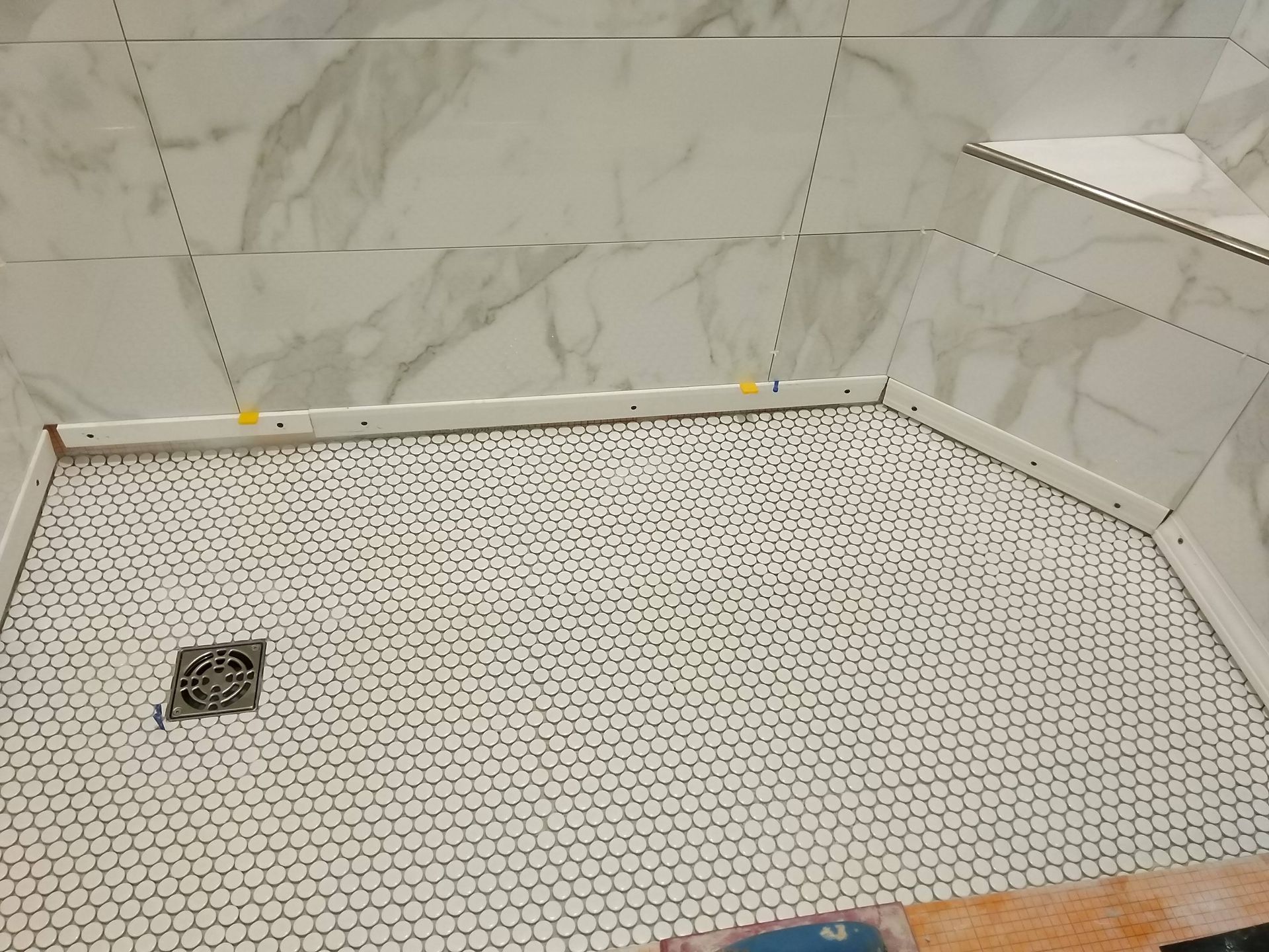 Small tiled shower stall with a hex tile floor, marble-look walls, and a drain in the corner.