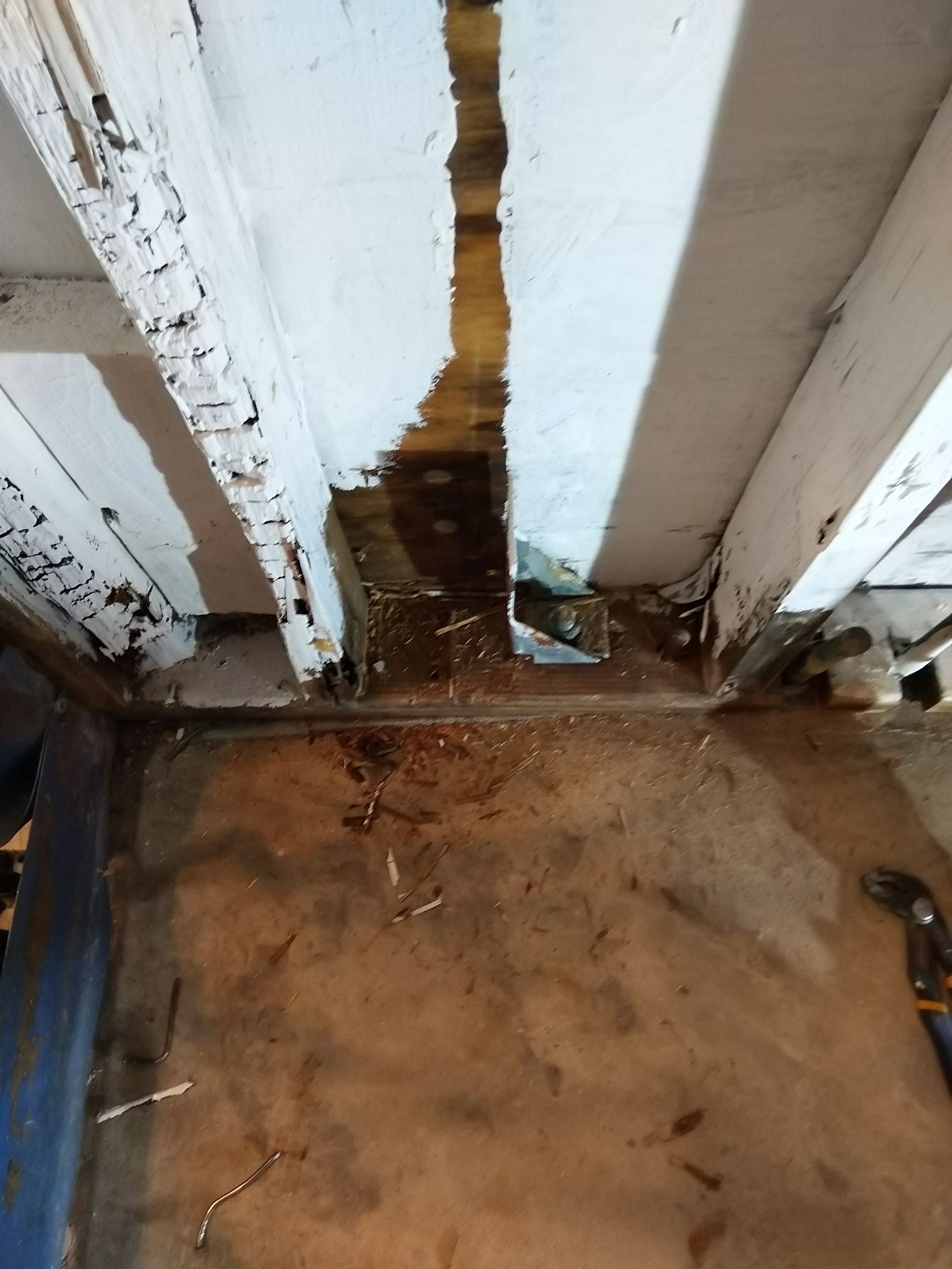 Water-damaged white wall and floor with dark stains, mold, and rust around the baseboards