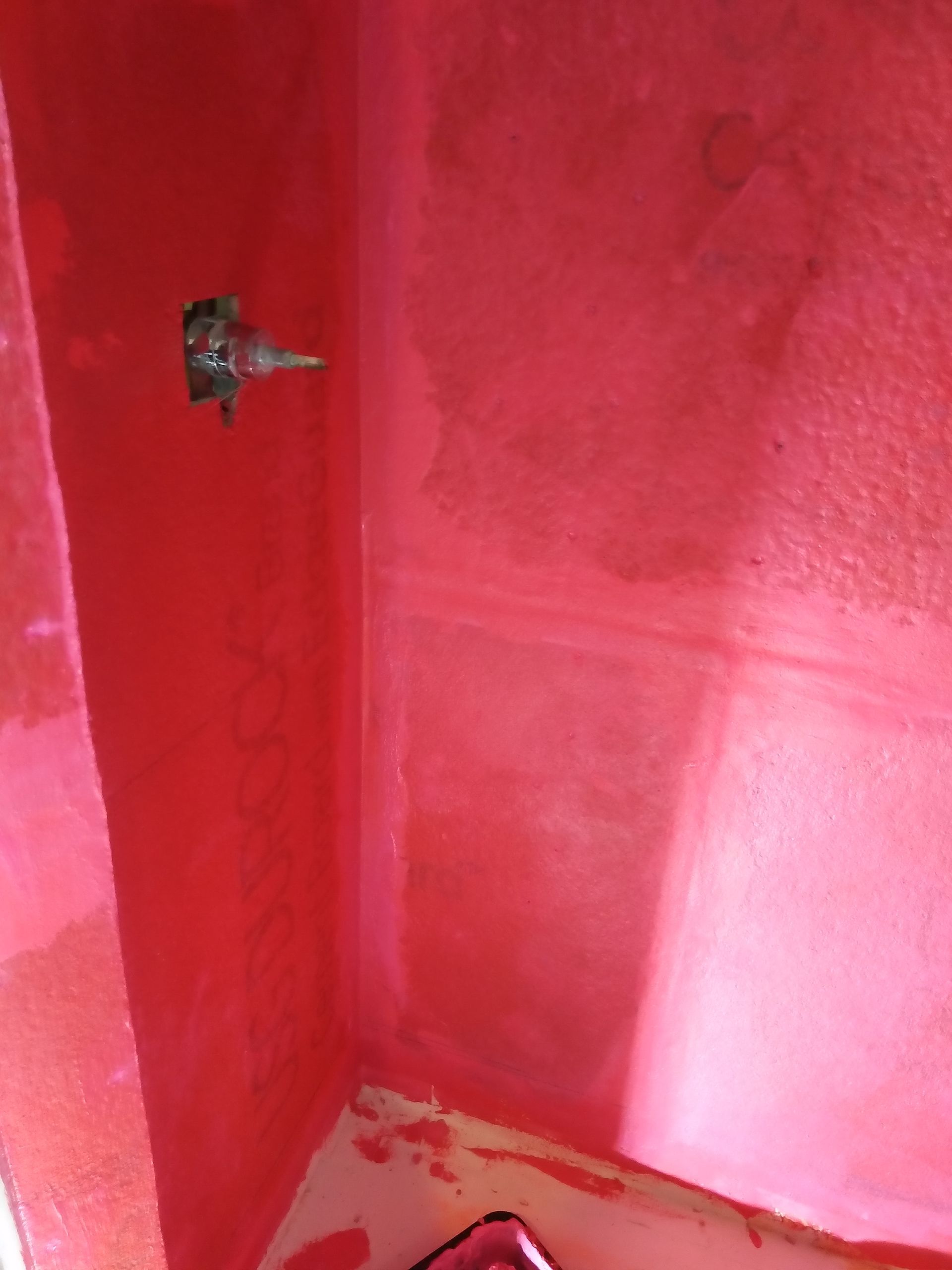 Pink-painted room corner with a rough wall patch and baseboard damage near the floor