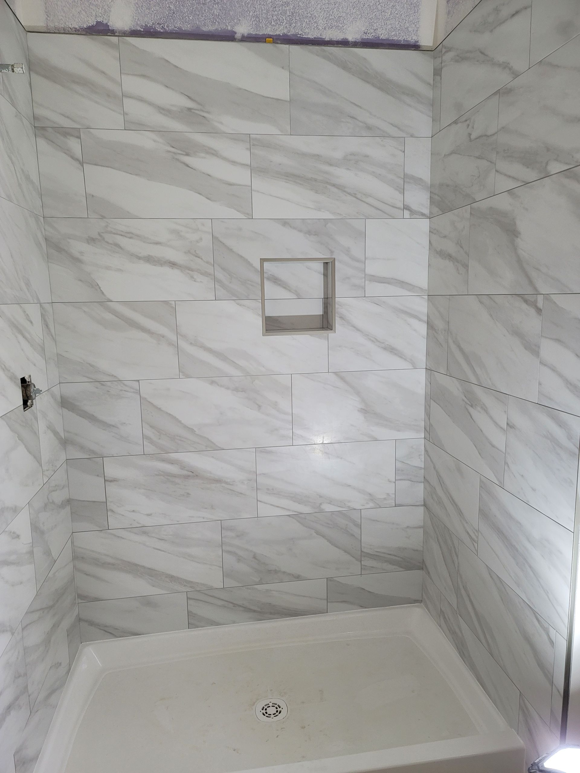 Empty tiled shower with marble-look walls and a small built-in shelf.