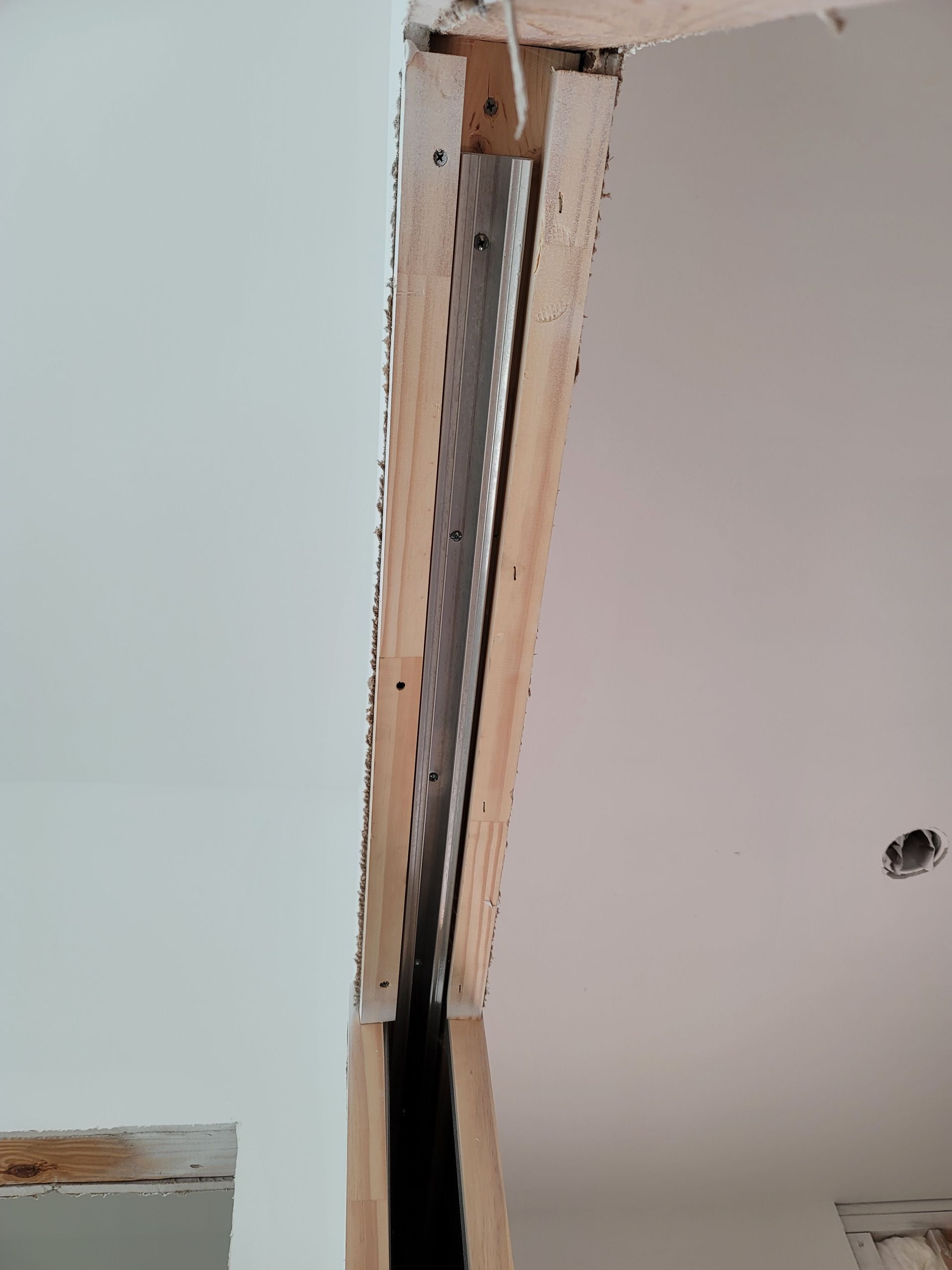 Damaged ceiling drywall around a vertical metal support beam, with exposed insulation and cracks
