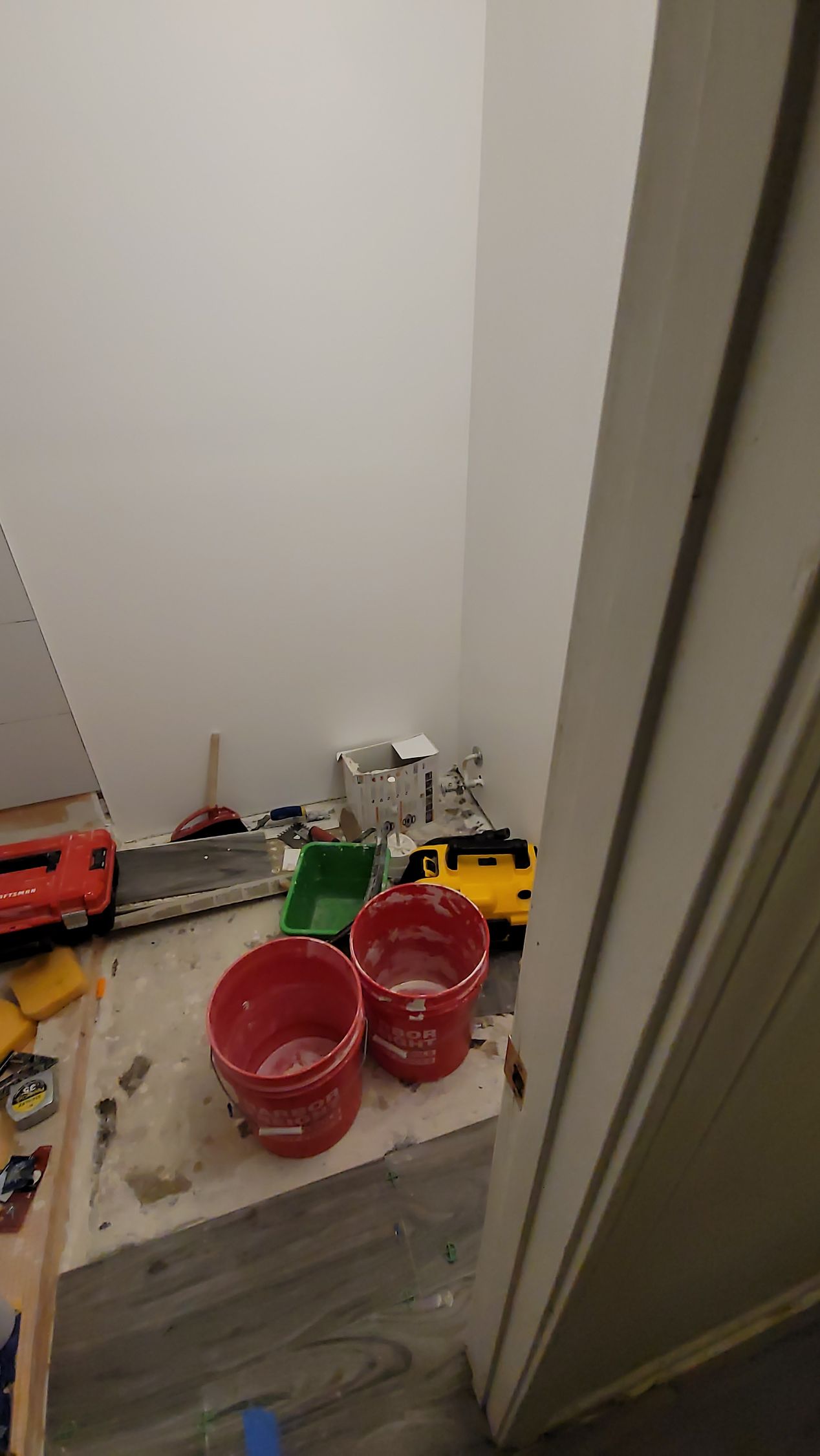 Toy cars and red cups scattered on a floor beside an open door and wall.