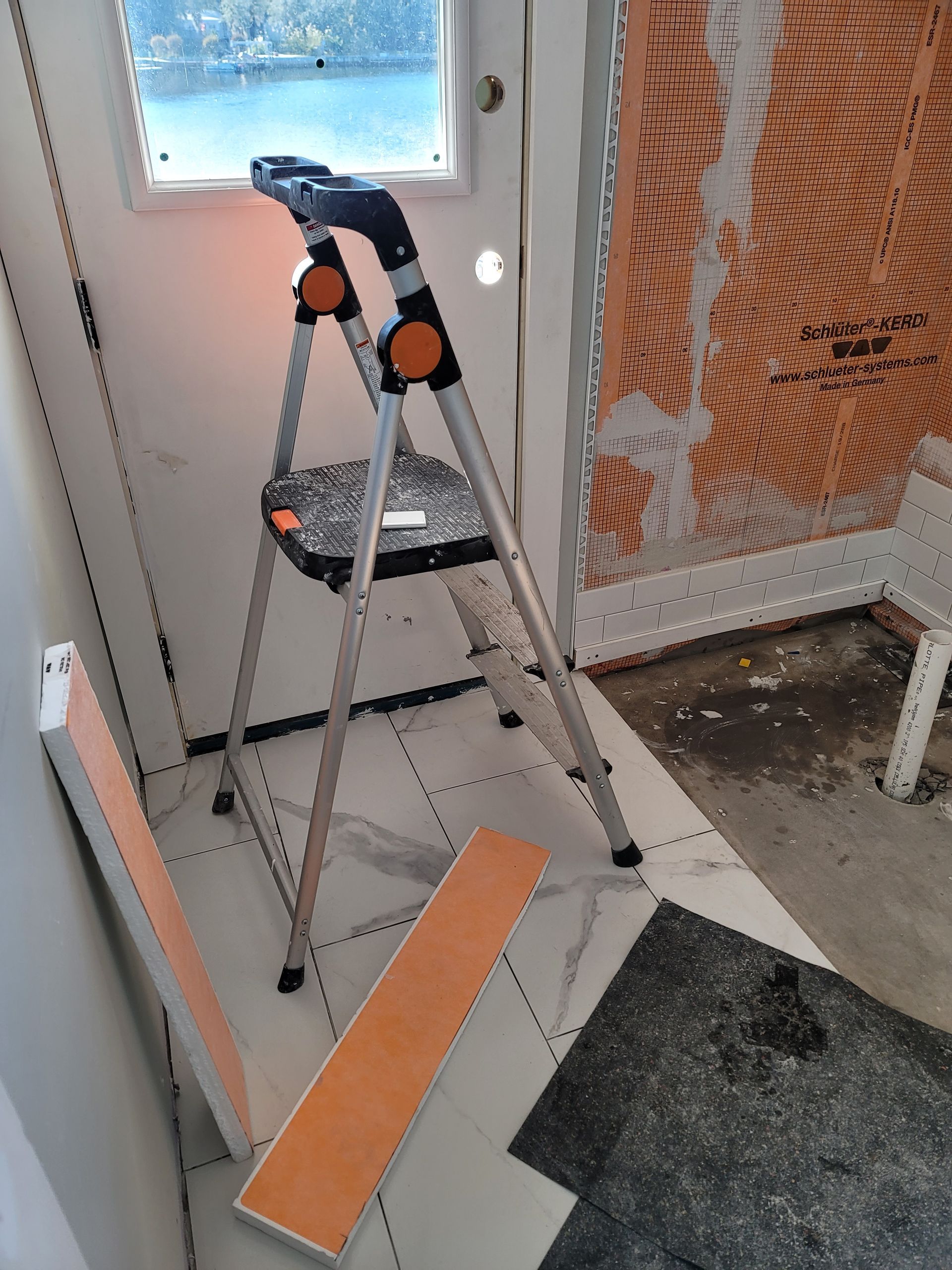 Step ladder beside a white door under renovation, with orange trim and construction debris on the floor.