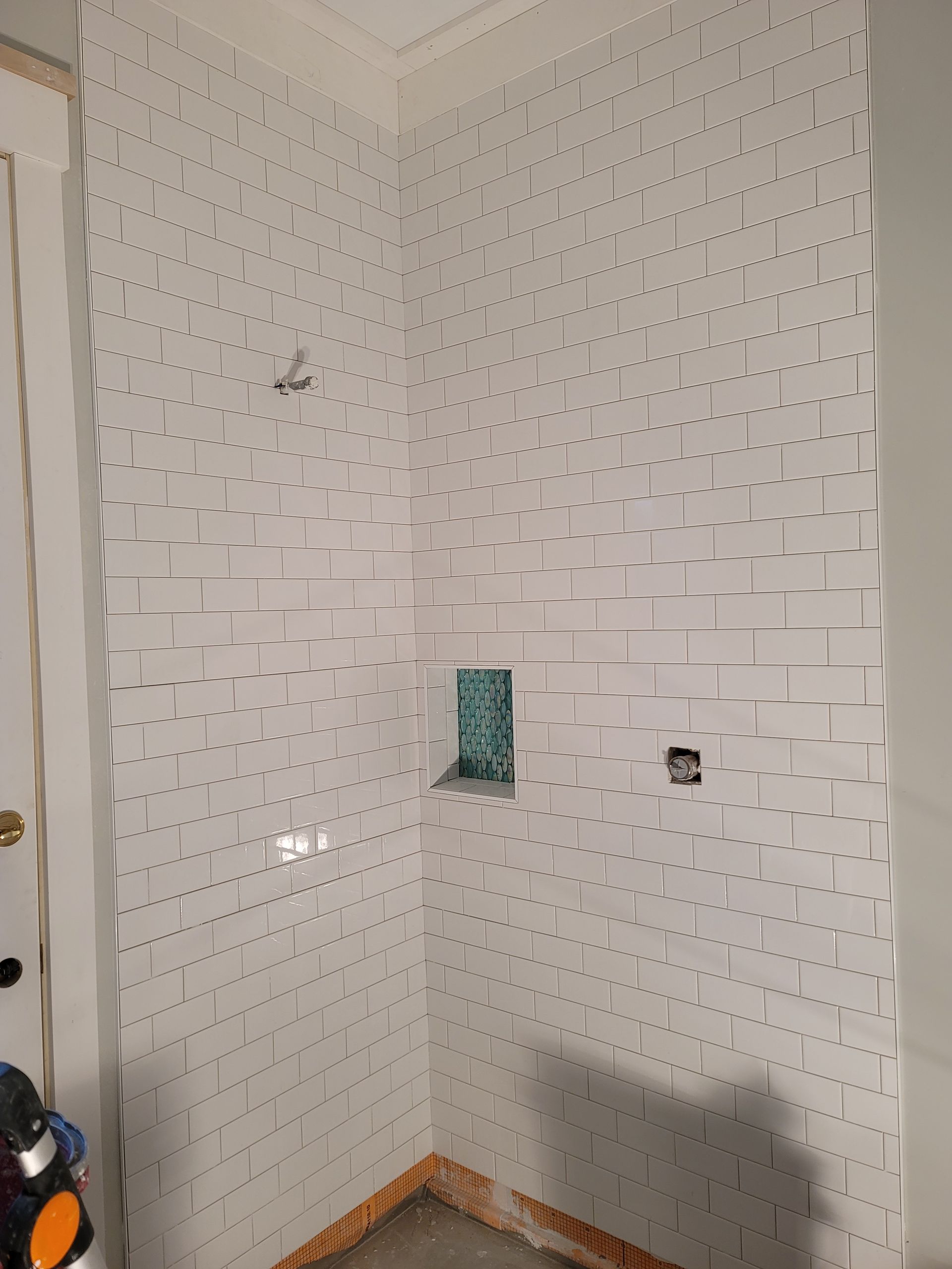 Empty white-tiled corner of a room with a small wall niche and exposed outlet openings.