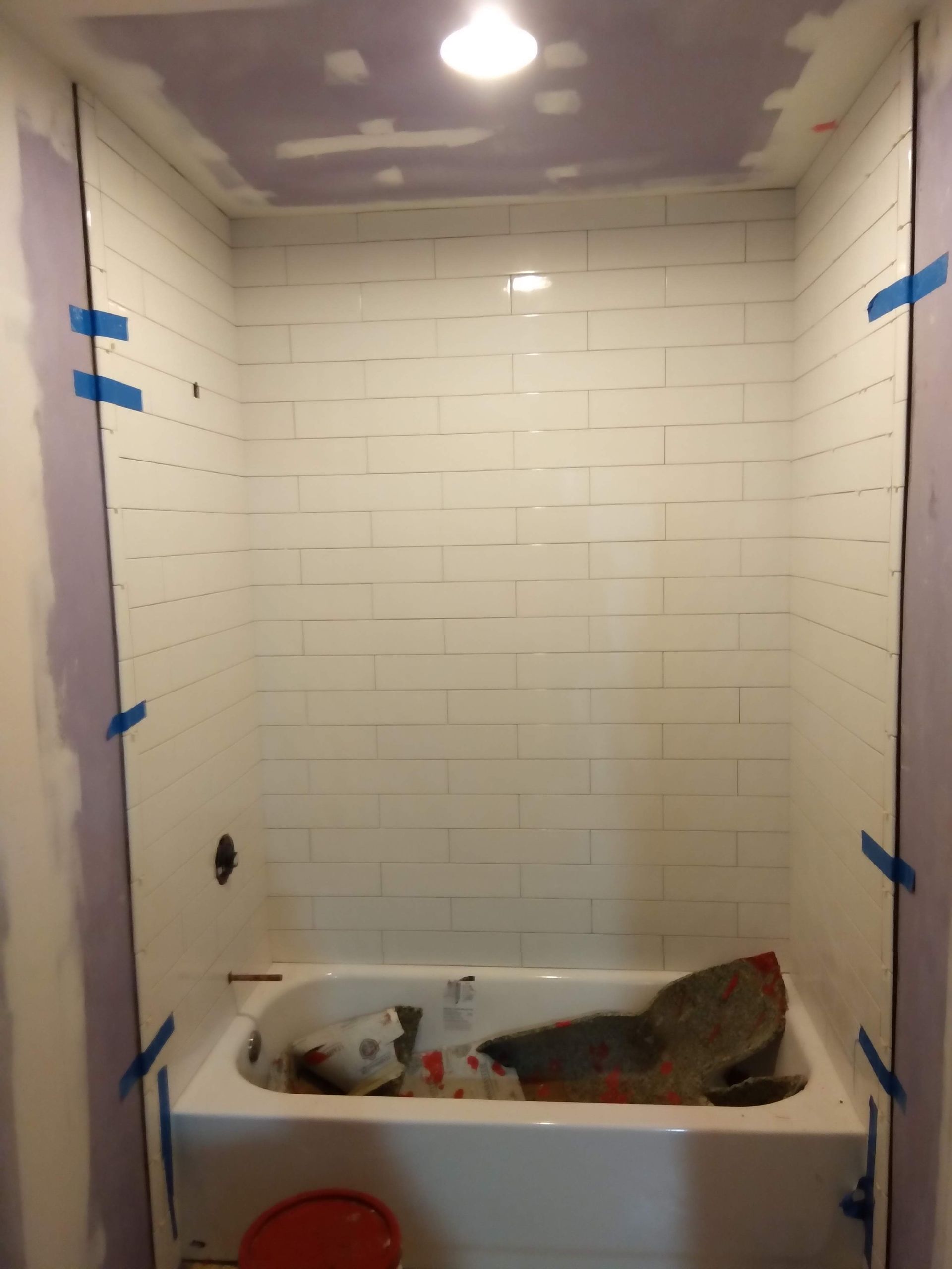 Bathroom shower in progress with taped wall panels, a bathtub, and a red bucket on the floor.