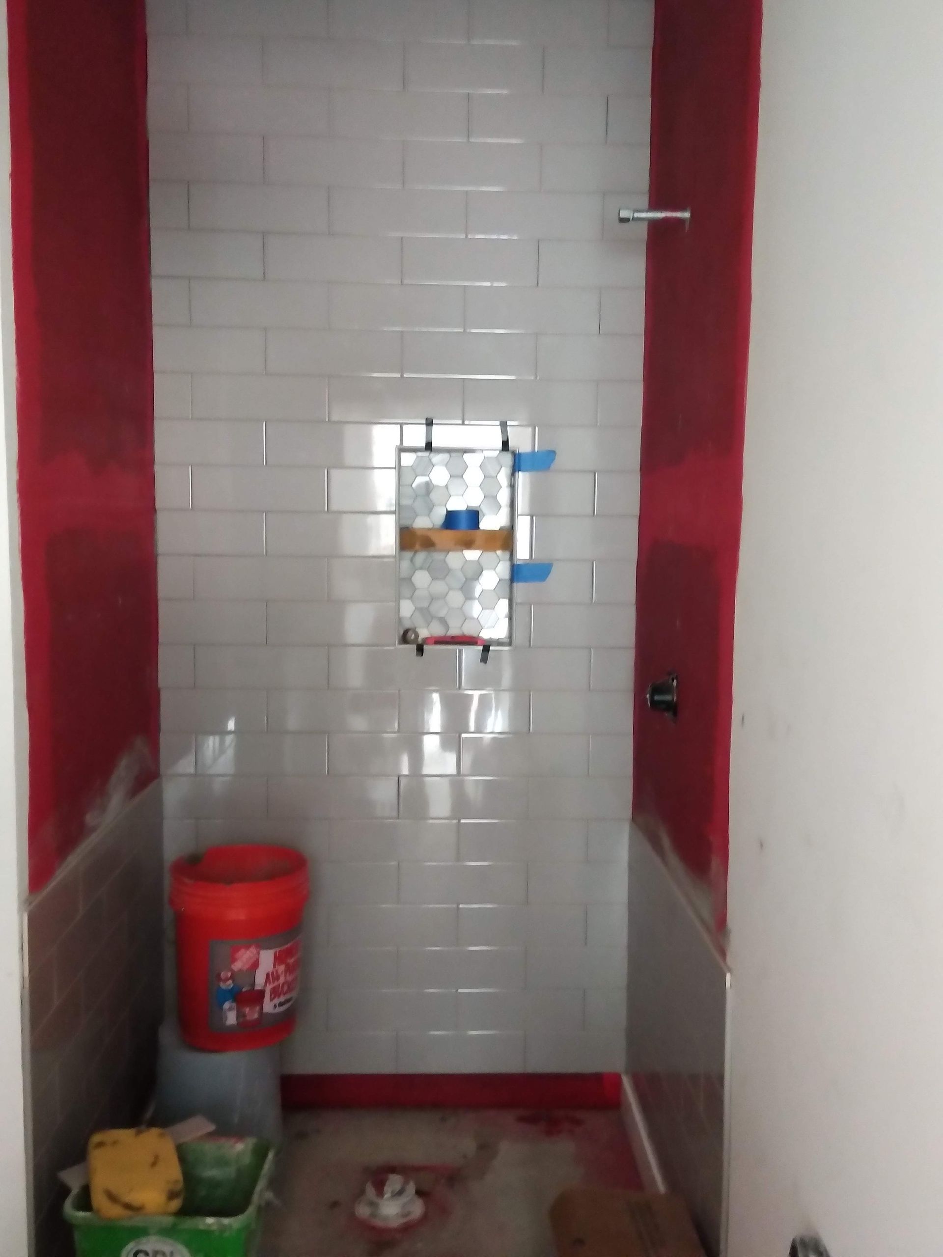 Narrow tiled restroom with a wall-mounted sink, red trim, and cleaning bucket on the floor