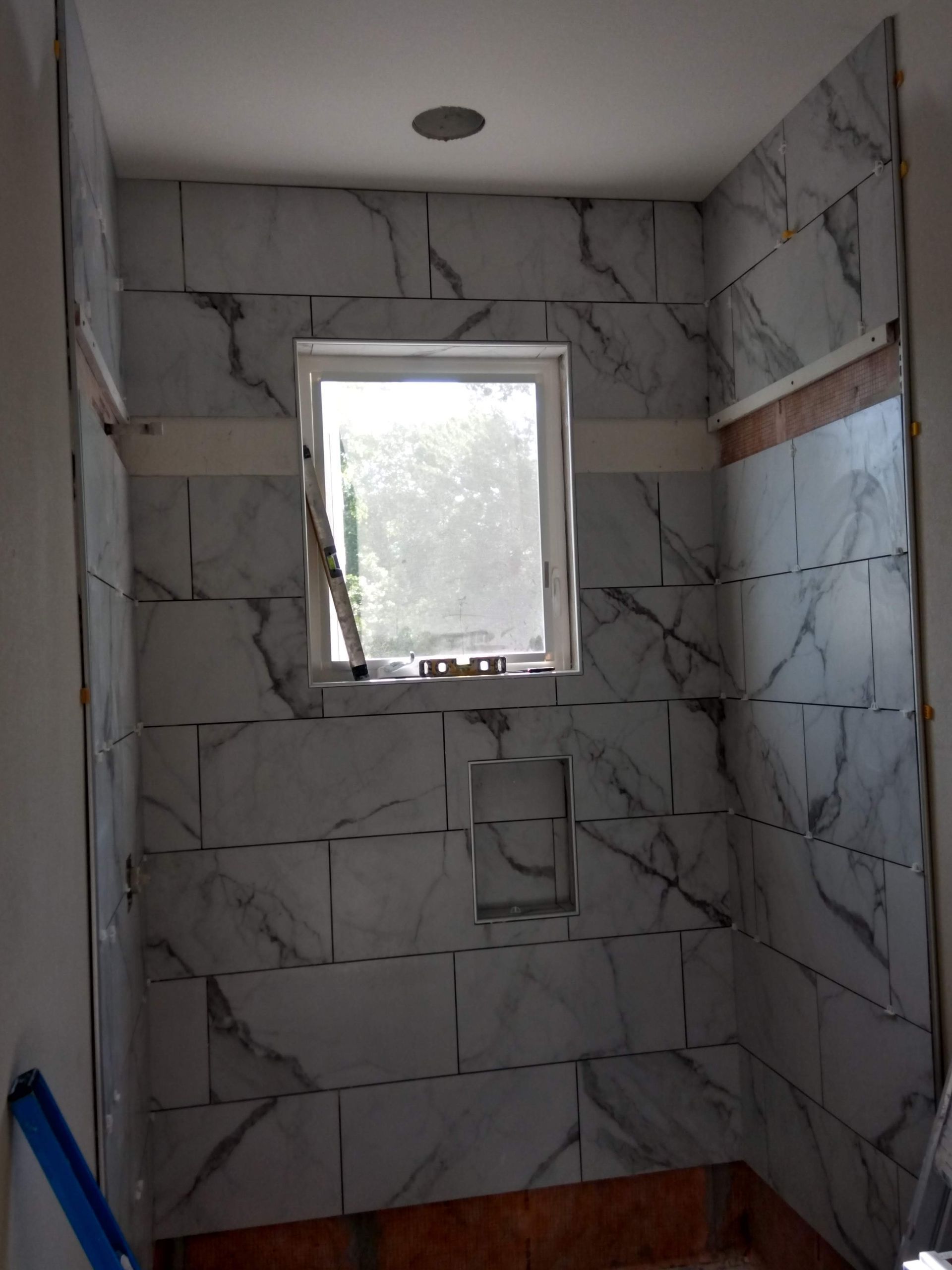 Tiled shower stall under construction with a small frosted window and recessed ceiling light