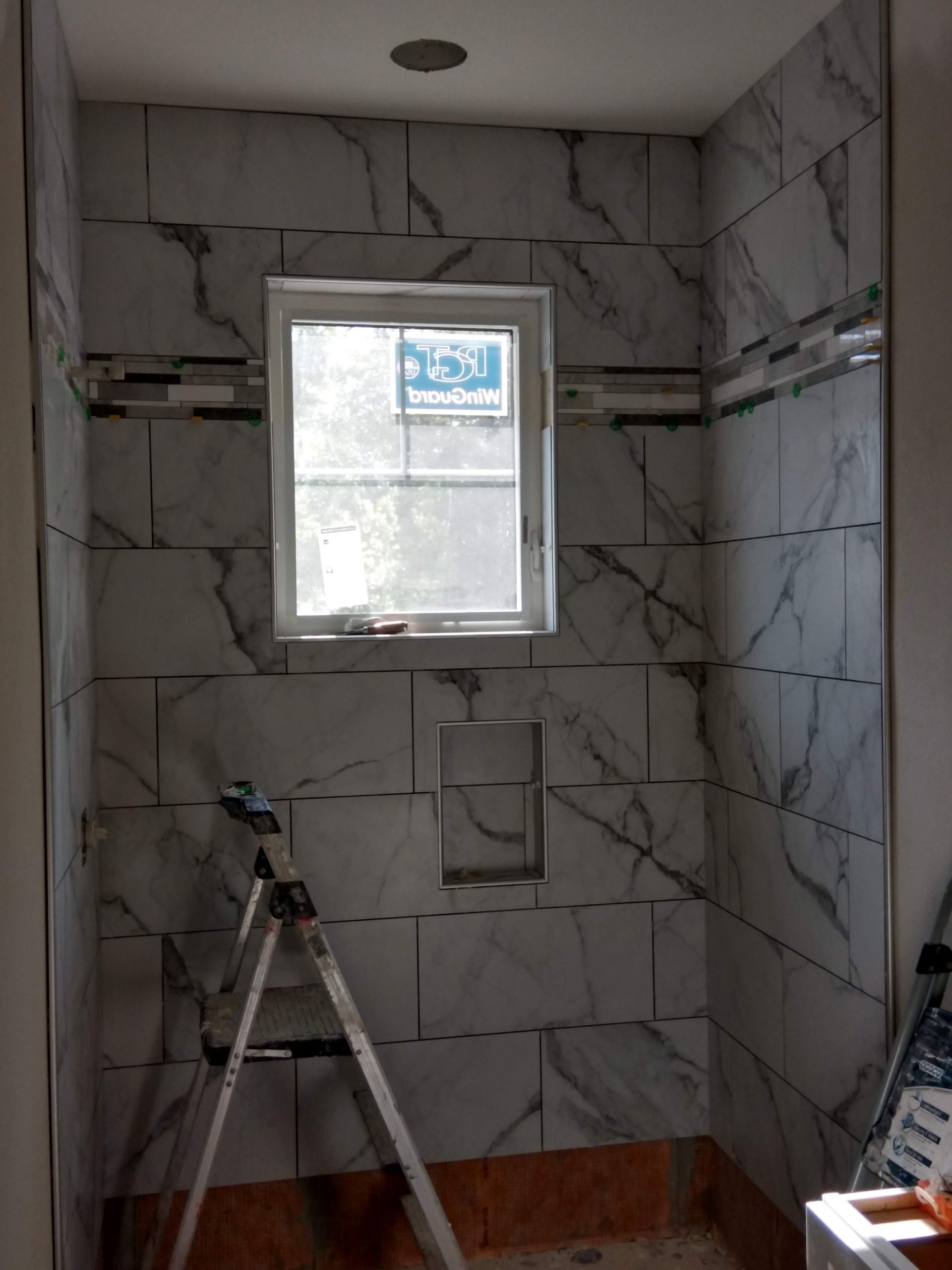 Bathroom under construction with tiled shower walls, a window, and a ladder inside the stall