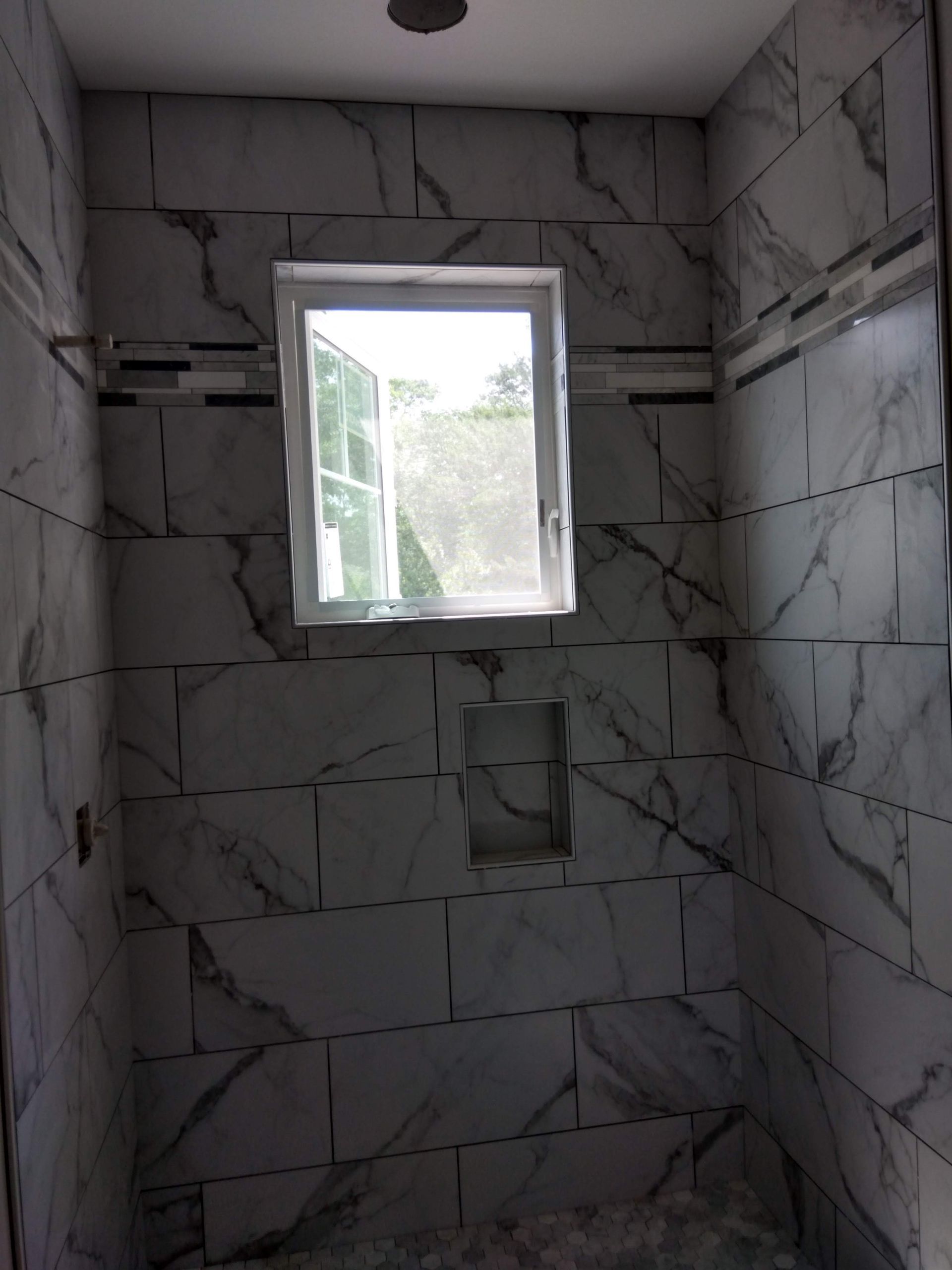 Small marble-tiled shower stall with a window letting in daylight.