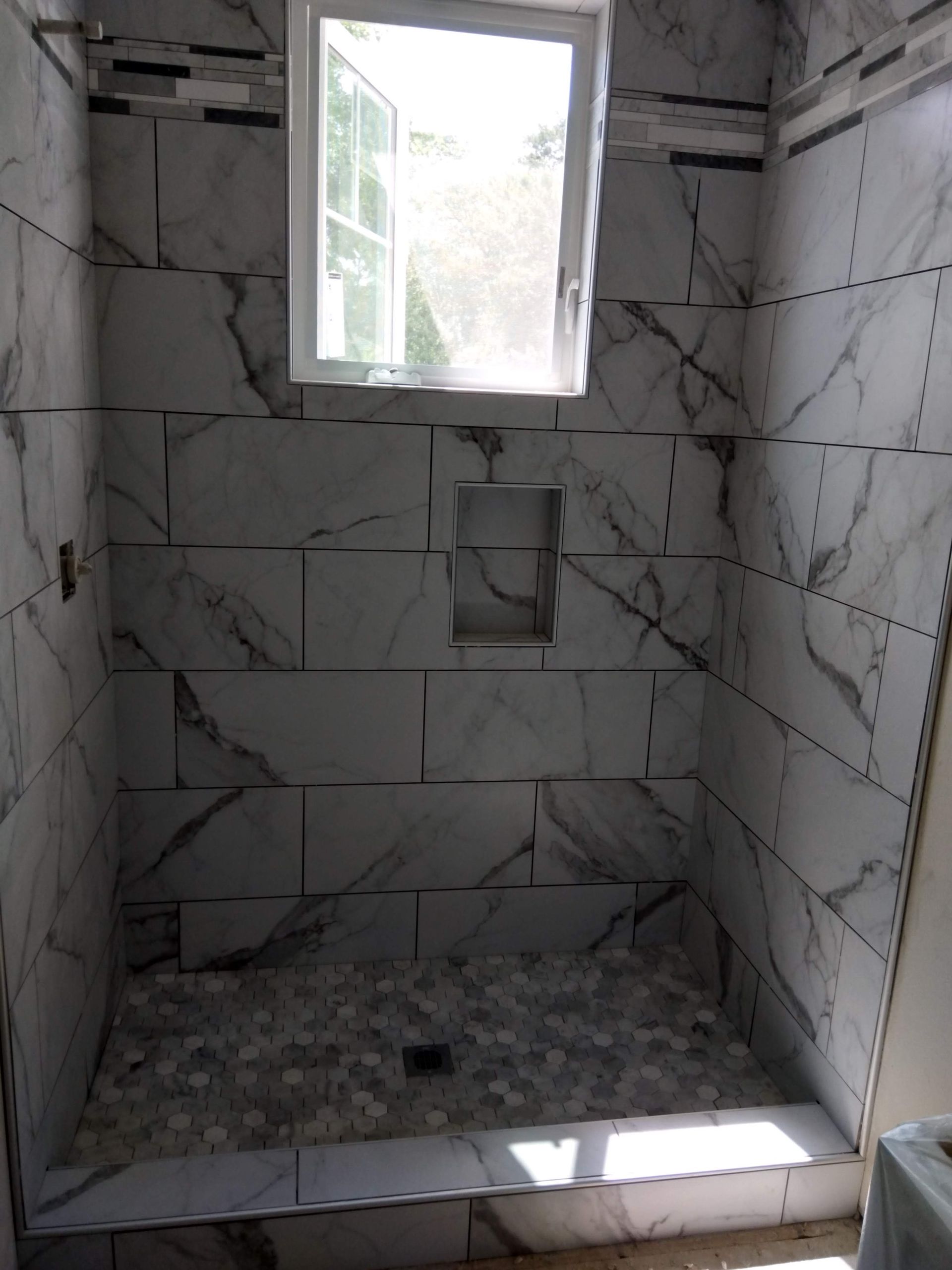 Tiled shower stall with a small frosted window and a white curb, under construction