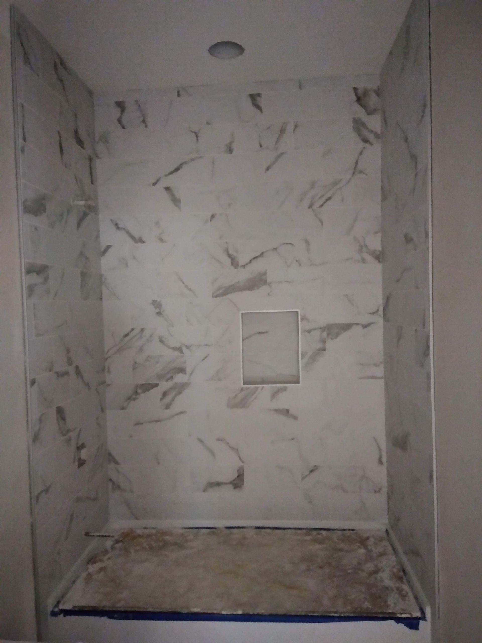 Empty tiled shower stall with a built-in bench and wall niche, viewed from the entrance