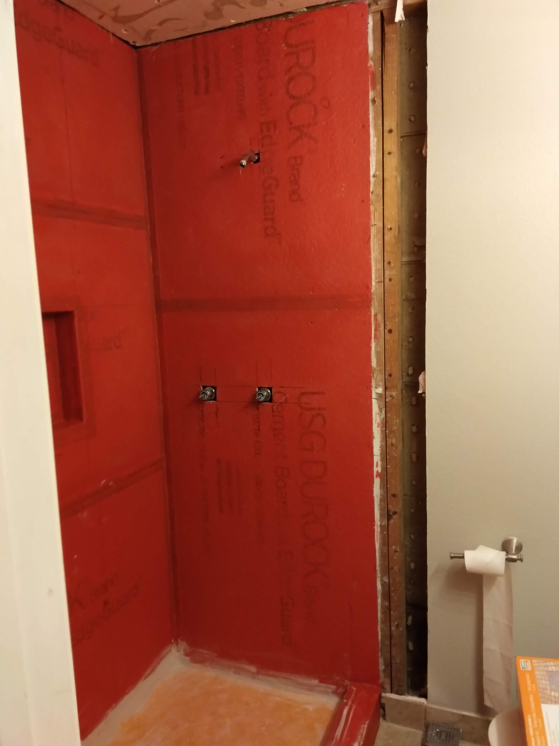 Red-tiled shower alcove under construction with exposed studs and plumbing connections.
