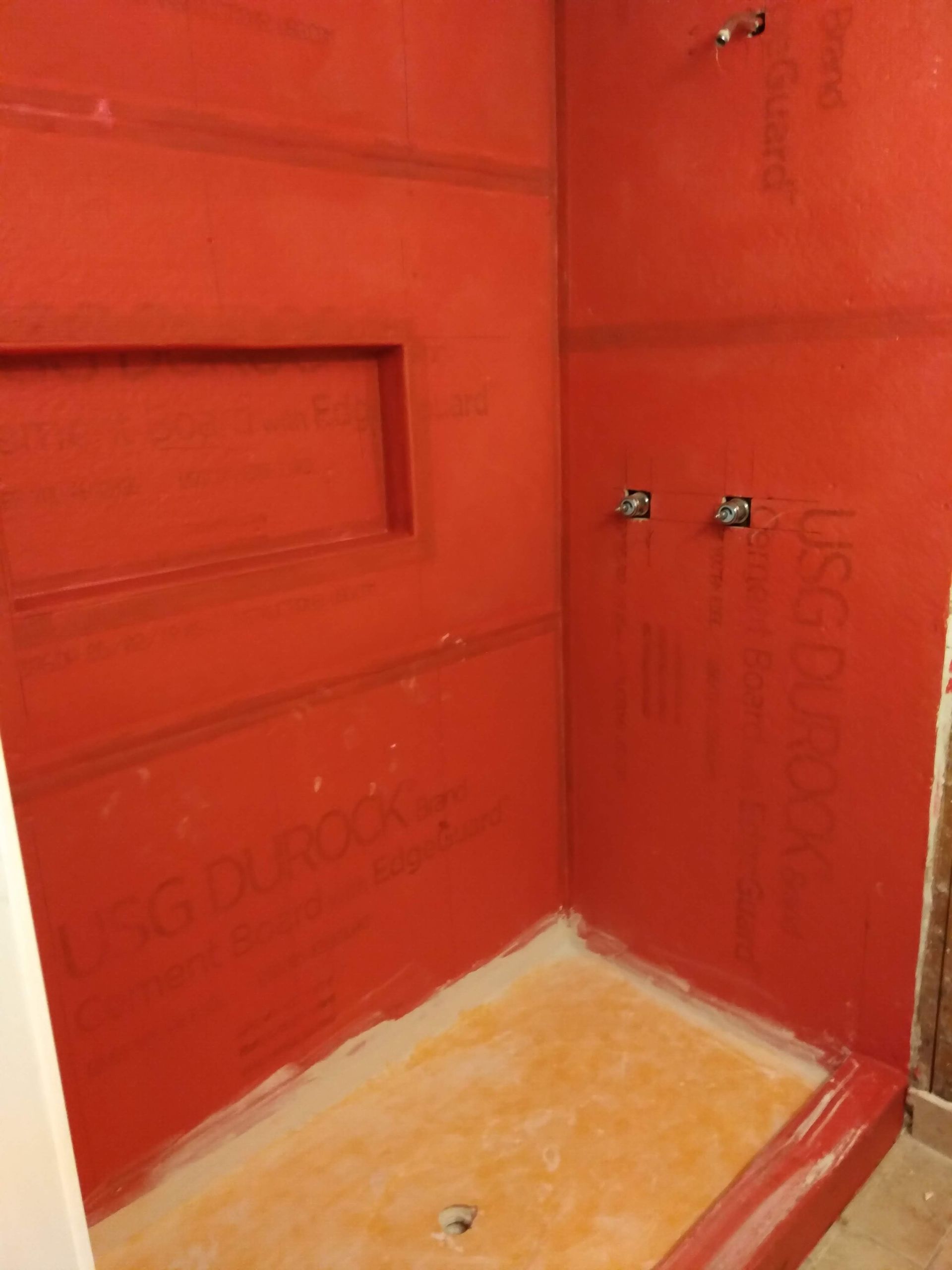 Red-tiled shower stall with a built-in shelf and faucet fixtures.