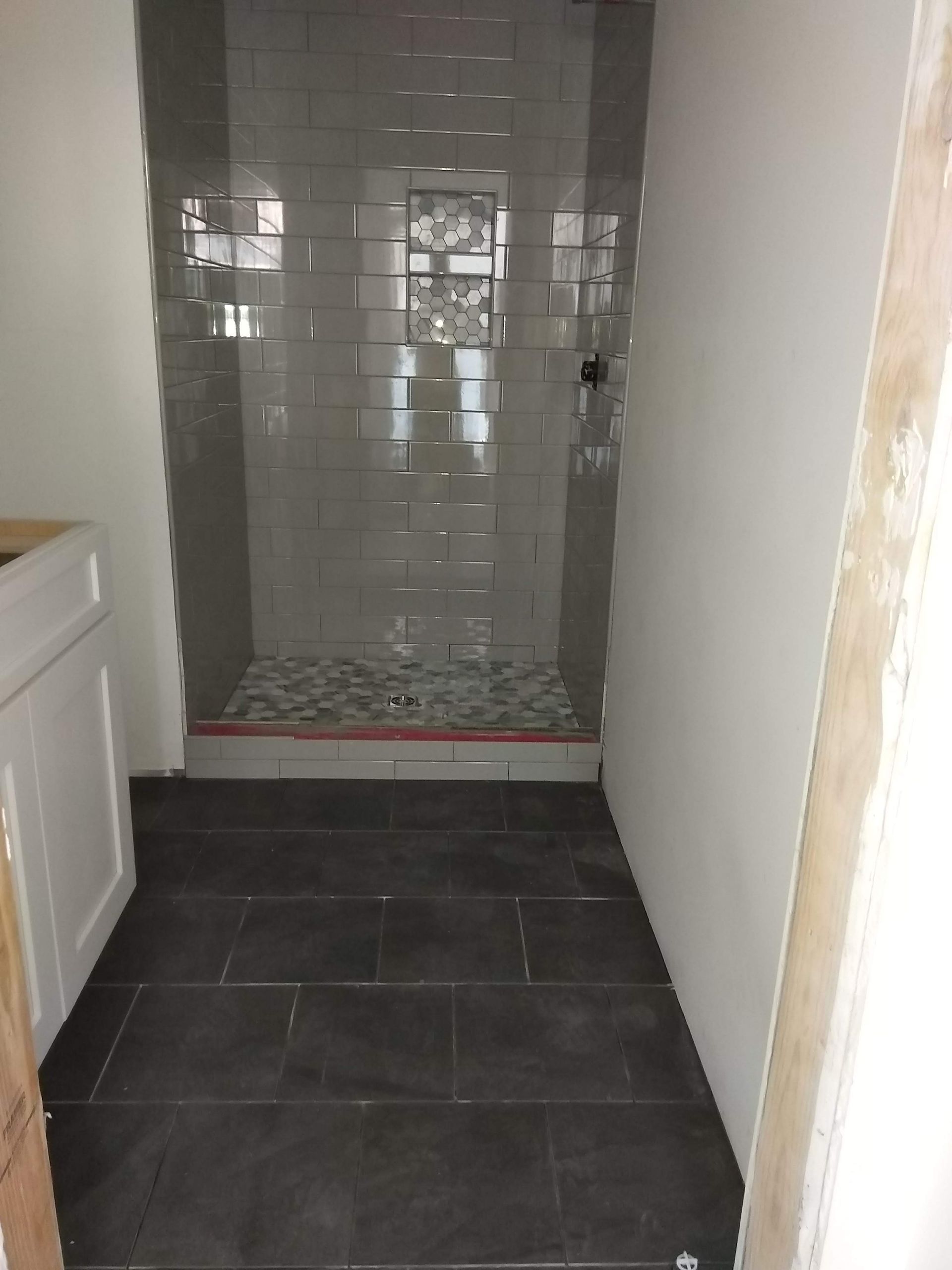 Narrow hallway leading to a tiled shower alcove with gray wall tiles and dark floor tiles