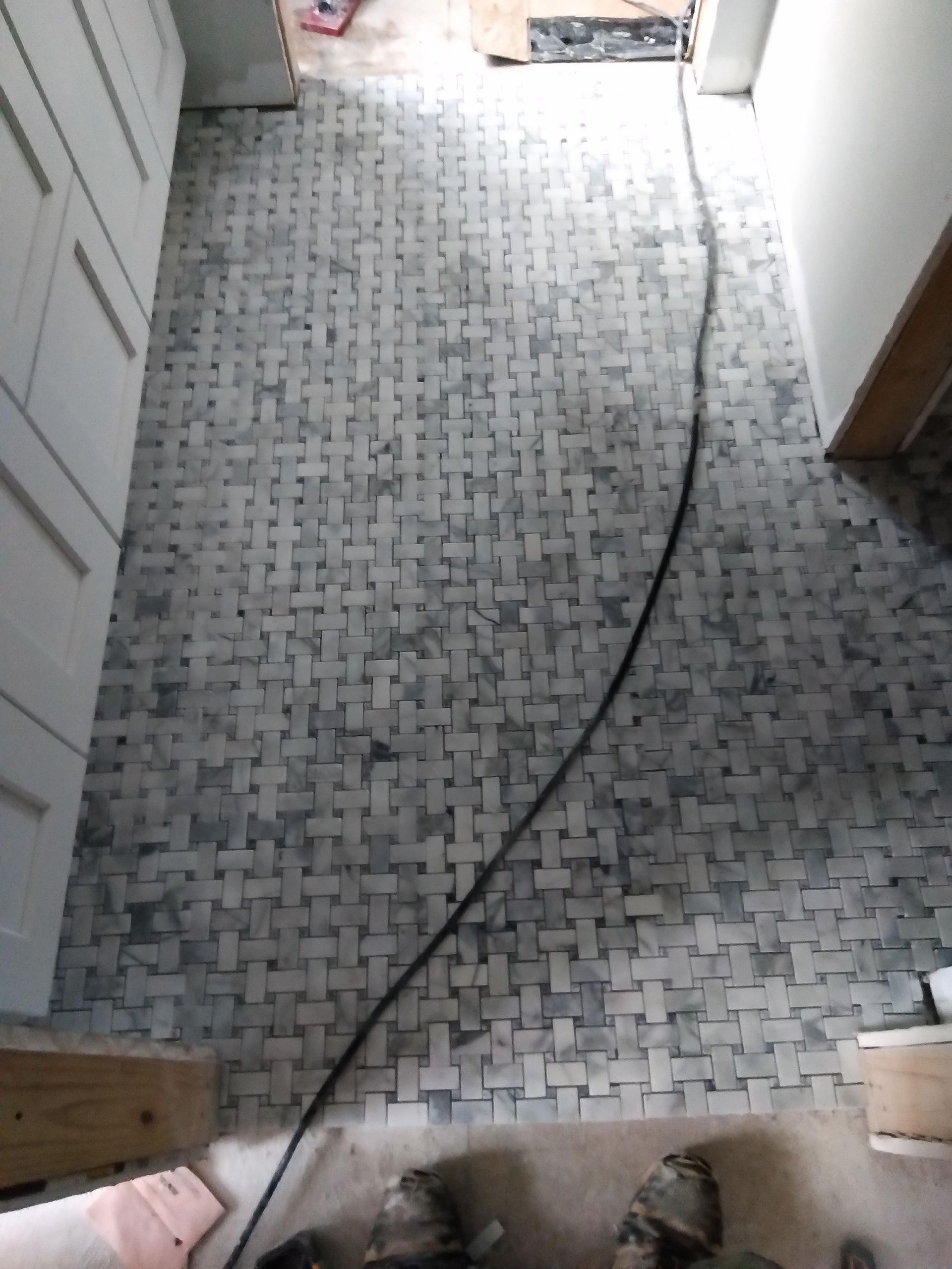 Narrow hallway with gray patterned floor and a black cable running across it, viewed from above.