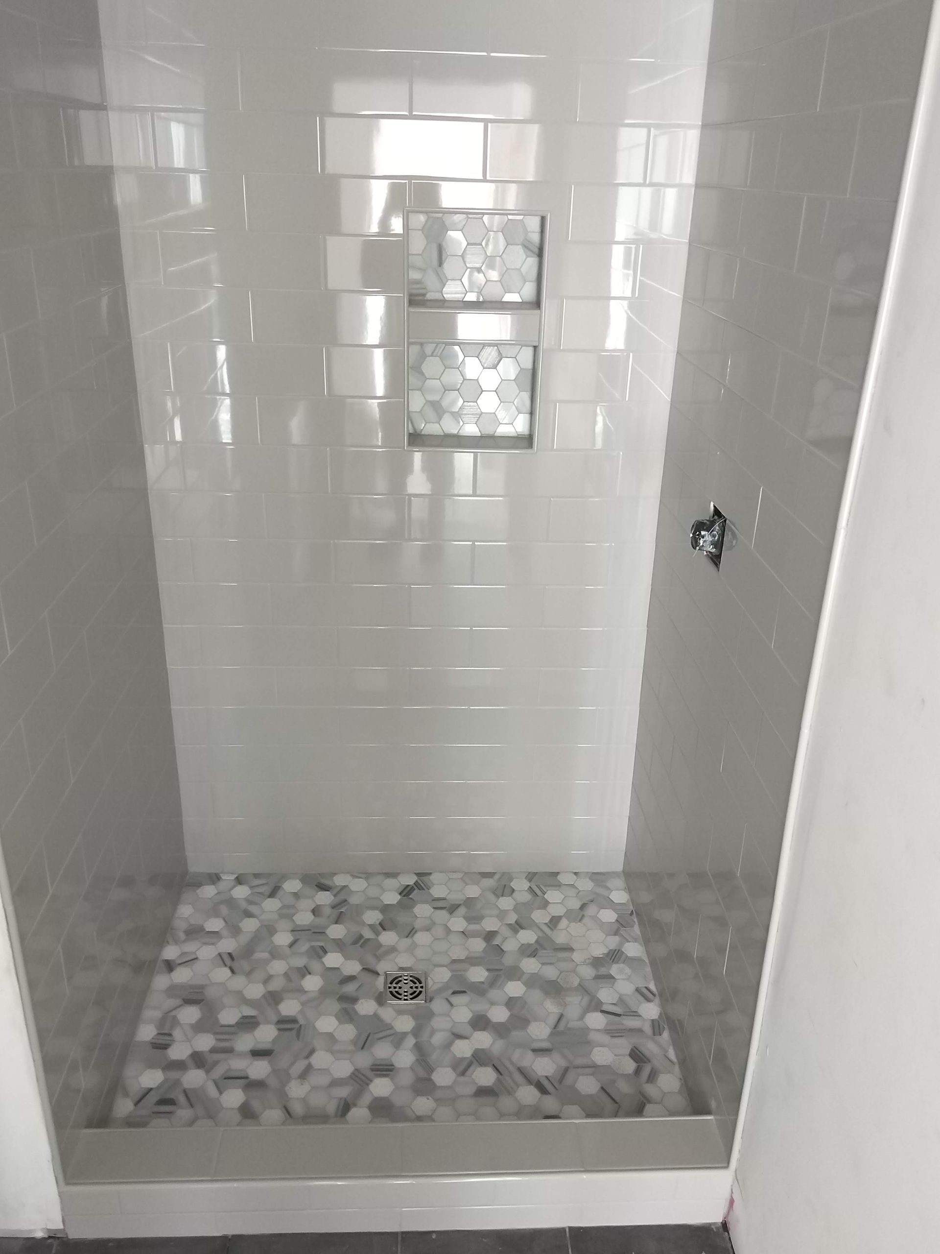 Small tiled shower stall with white walls and gray mosaic floor and shelf niches
