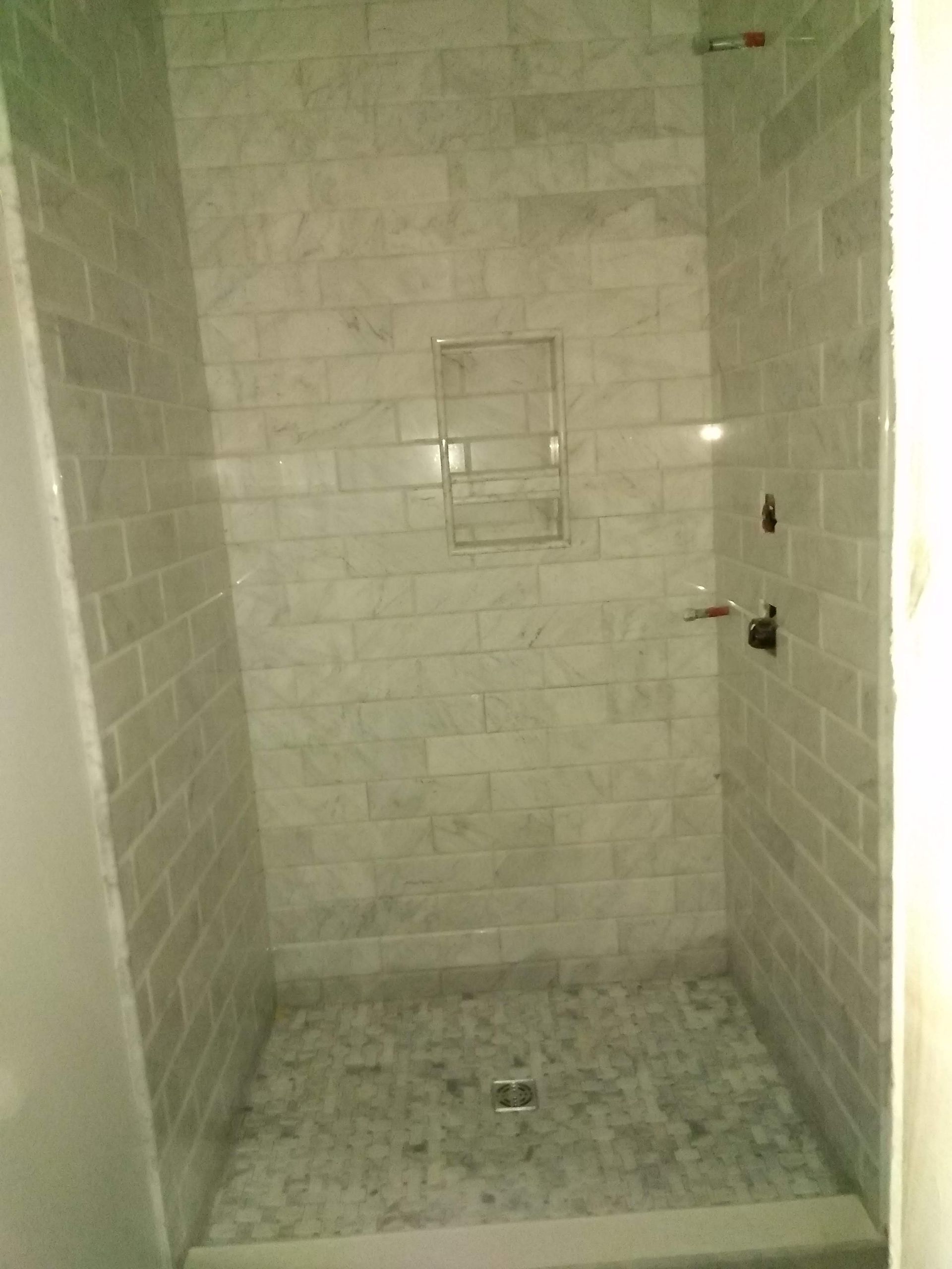Small tiled shower stall with a built-in shelf and floor drain.
