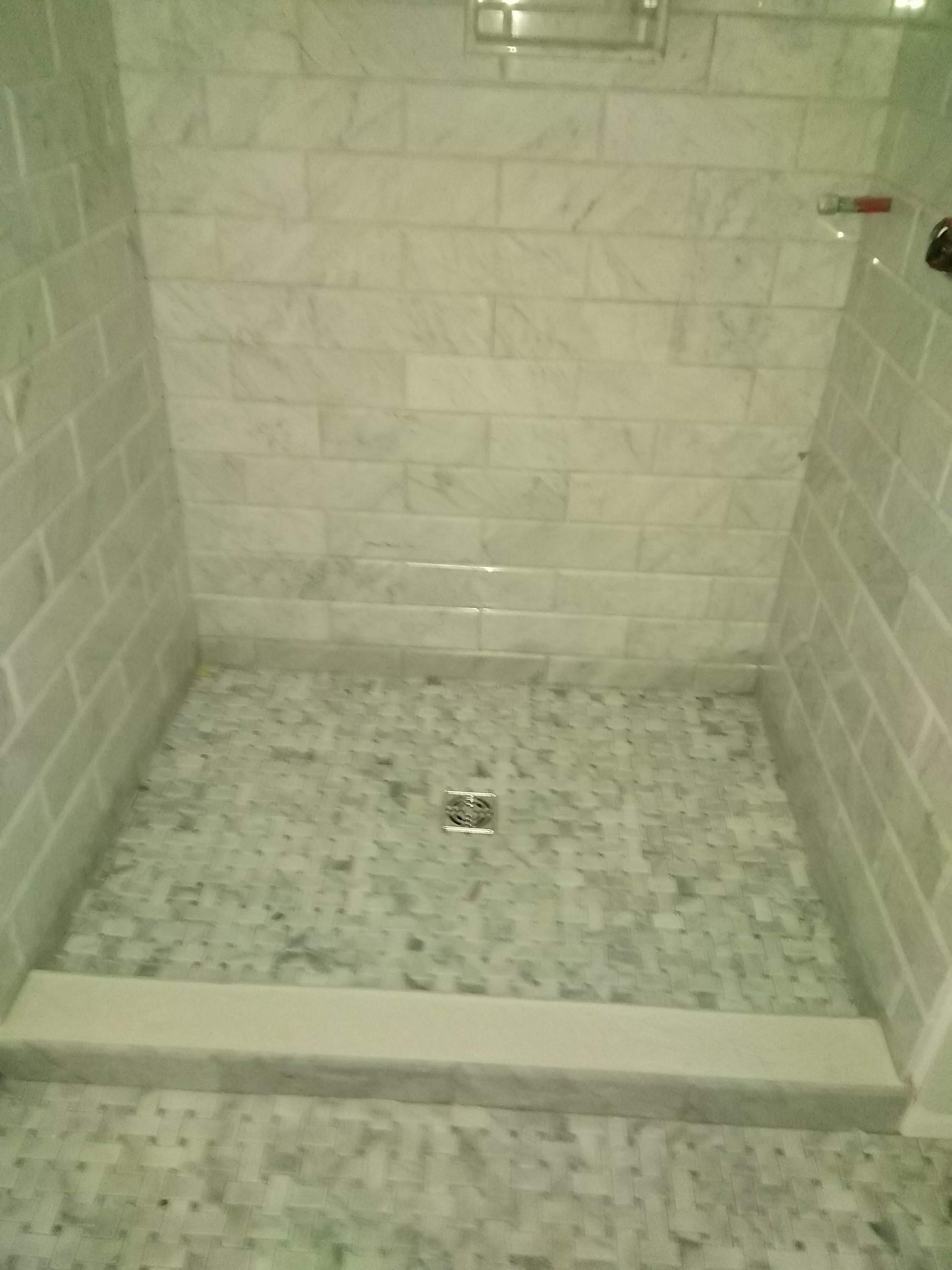 Small tiled shower stall with a low step and a central drain, seen from the entrance.