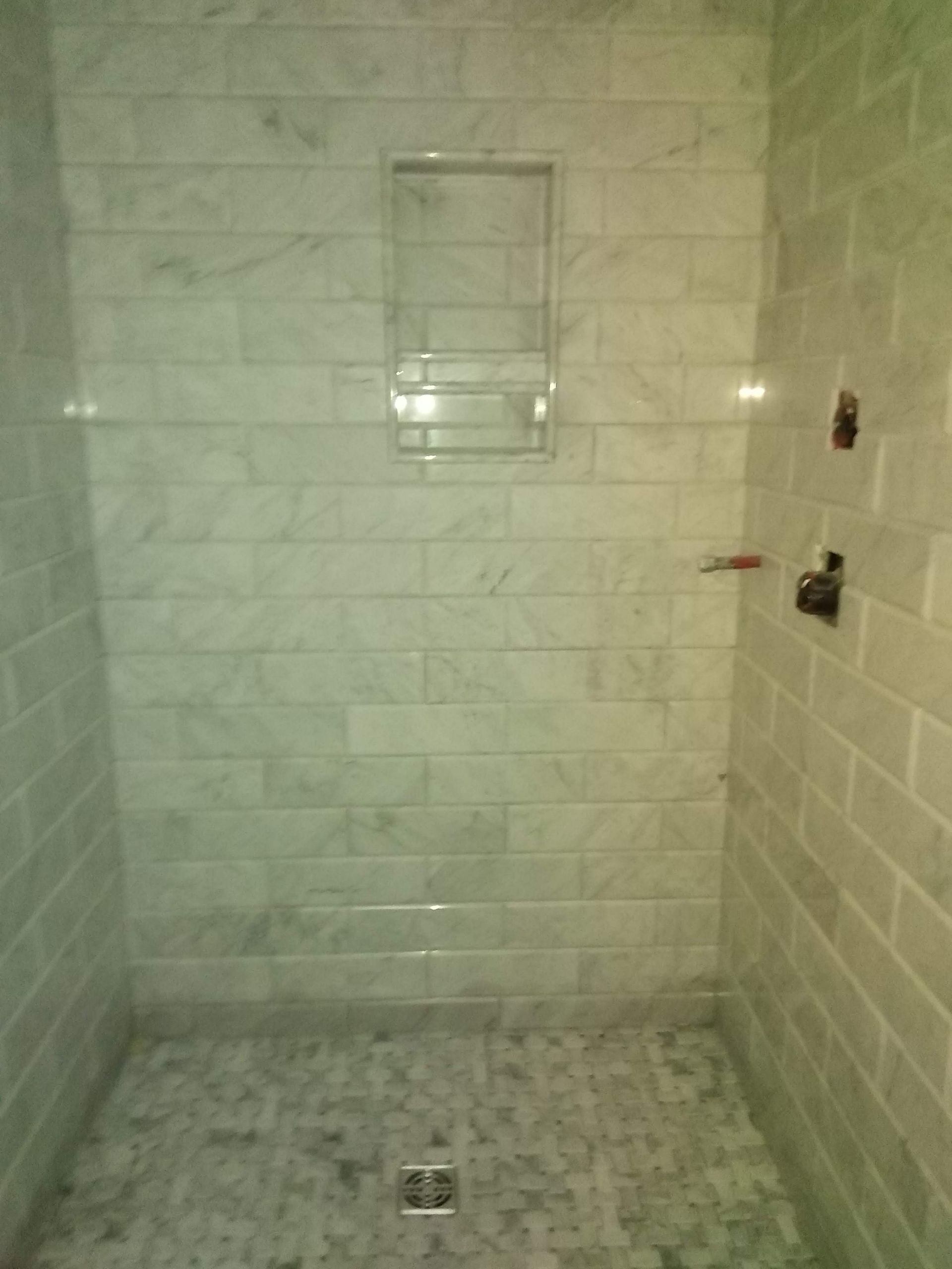 Empty tiled shower stall with a square drain and built-in soap holder.