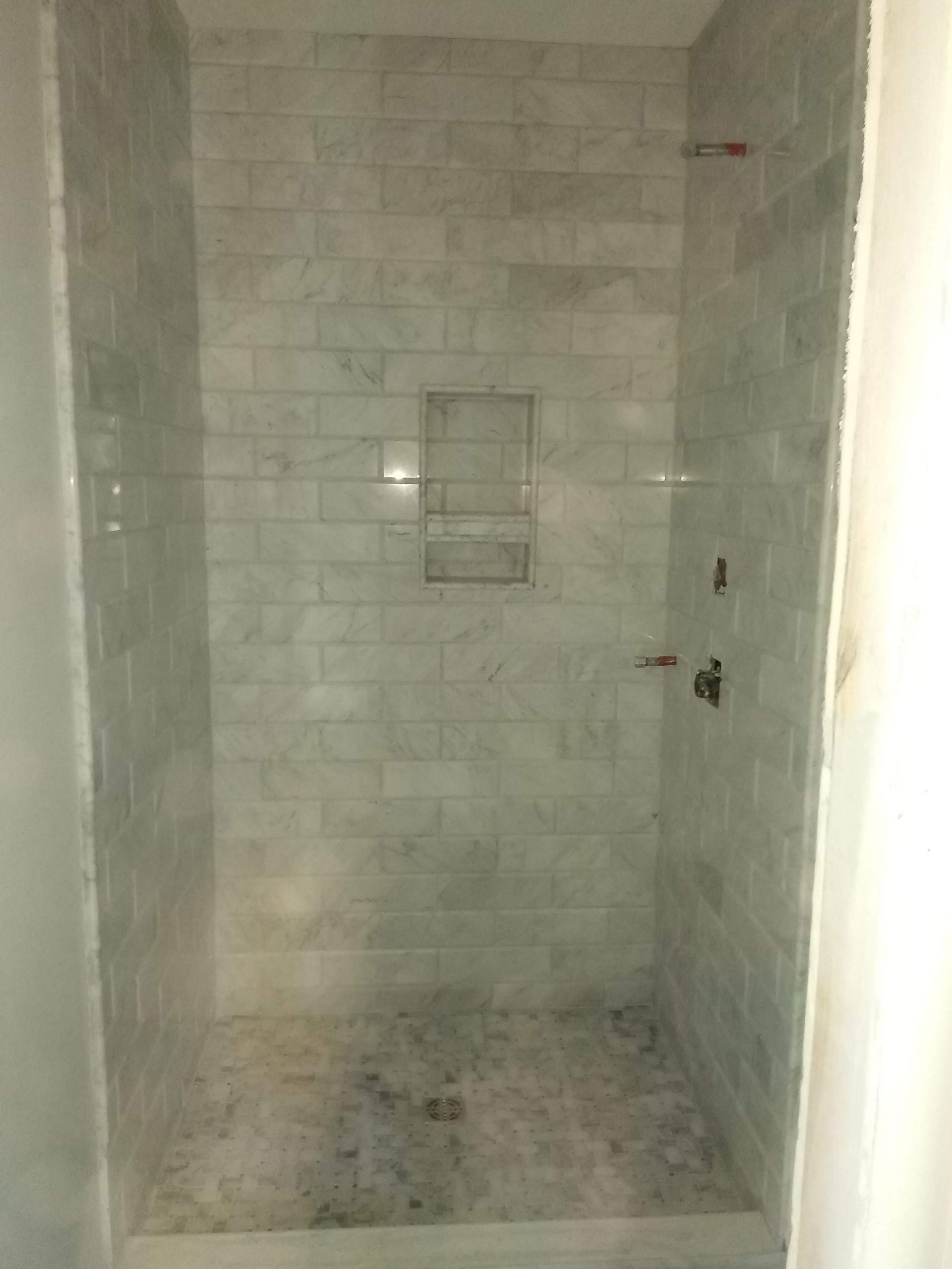 Empty tiled shower stall with a small recessed shelf and drain in the floor.