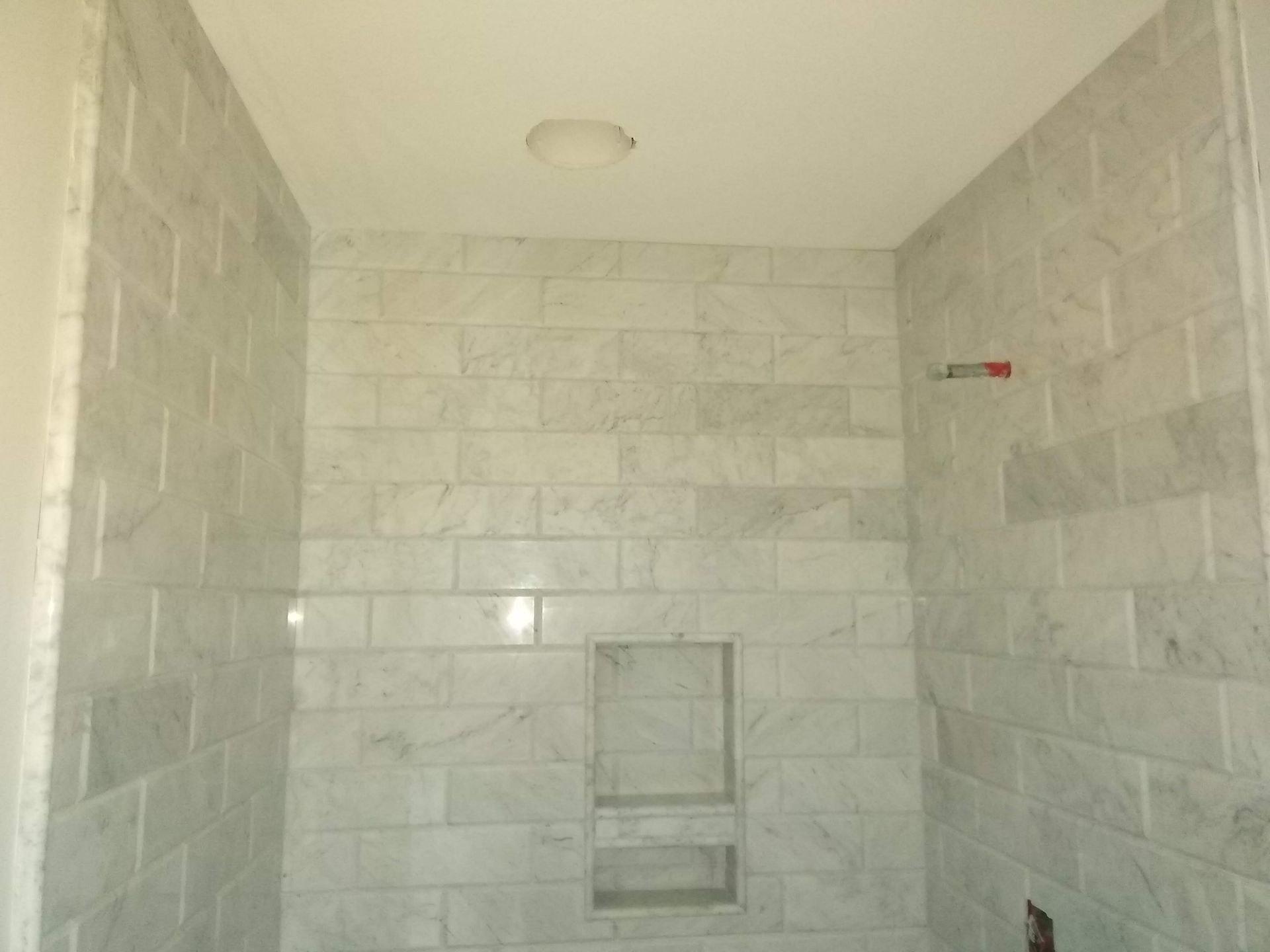 Empty white-tiled shower stall with a recessed shelf and small window niche