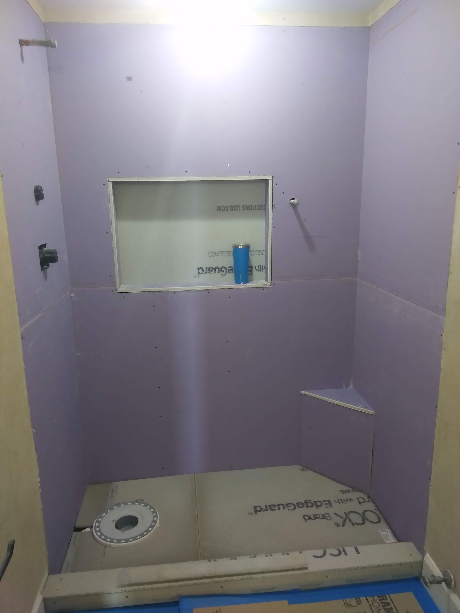 Small tiled shower stall under construction with lavender waterproofing and a recessed shelf.