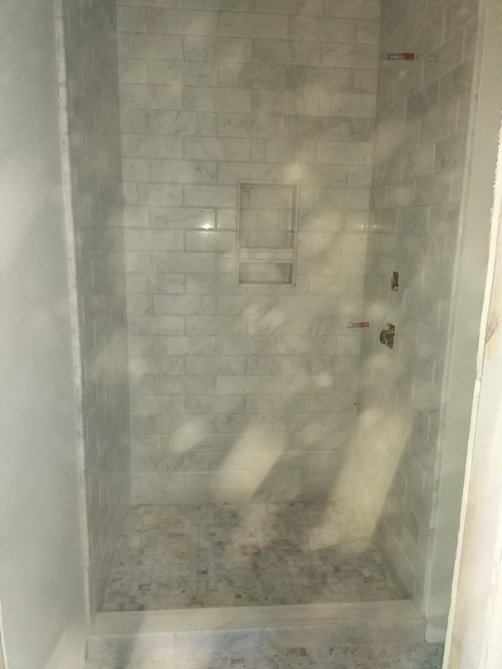 Empty tiled shower stall with frosted glass door and a shower handle on the right