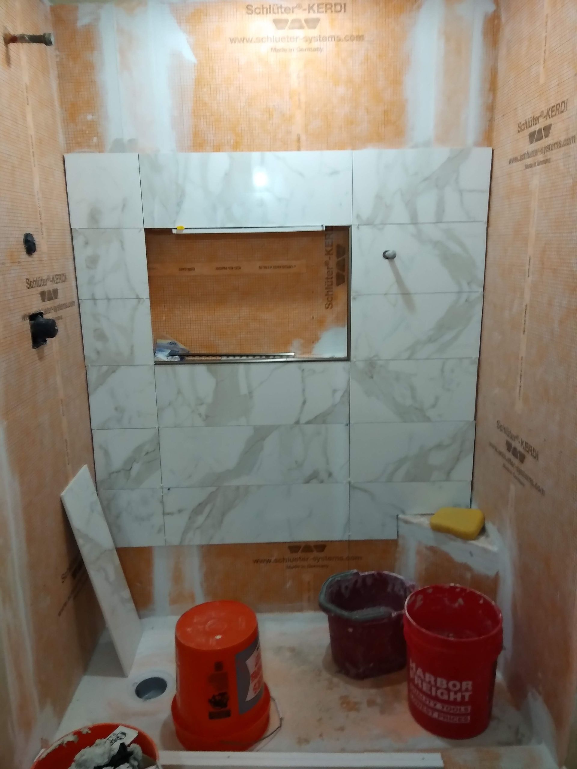 Small tiled shower under construction with buckets, tools, and unfinished wall panels.
