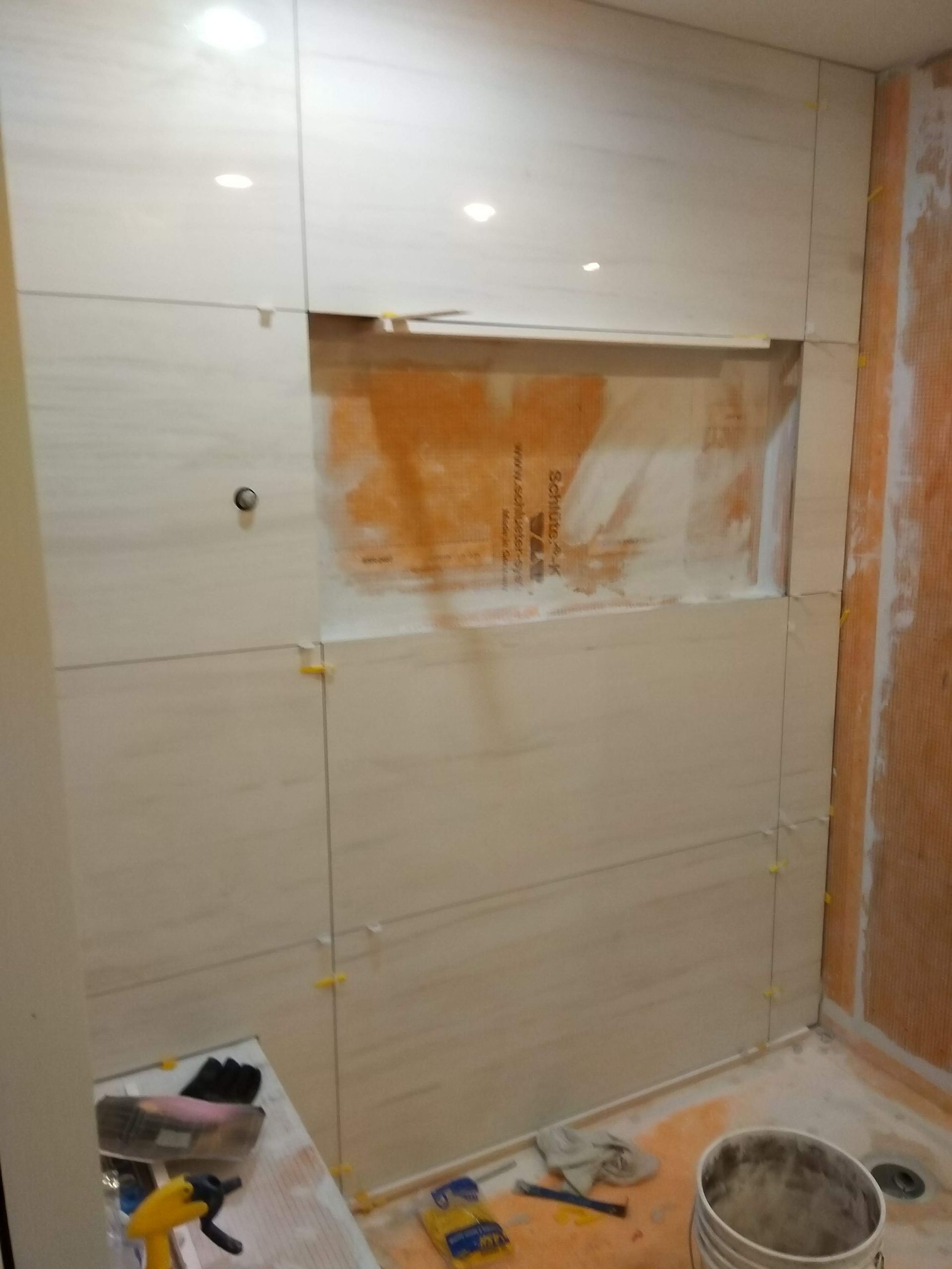 Partially tiled bathroom wall with exposed orange plaster and renovation tools on the floor