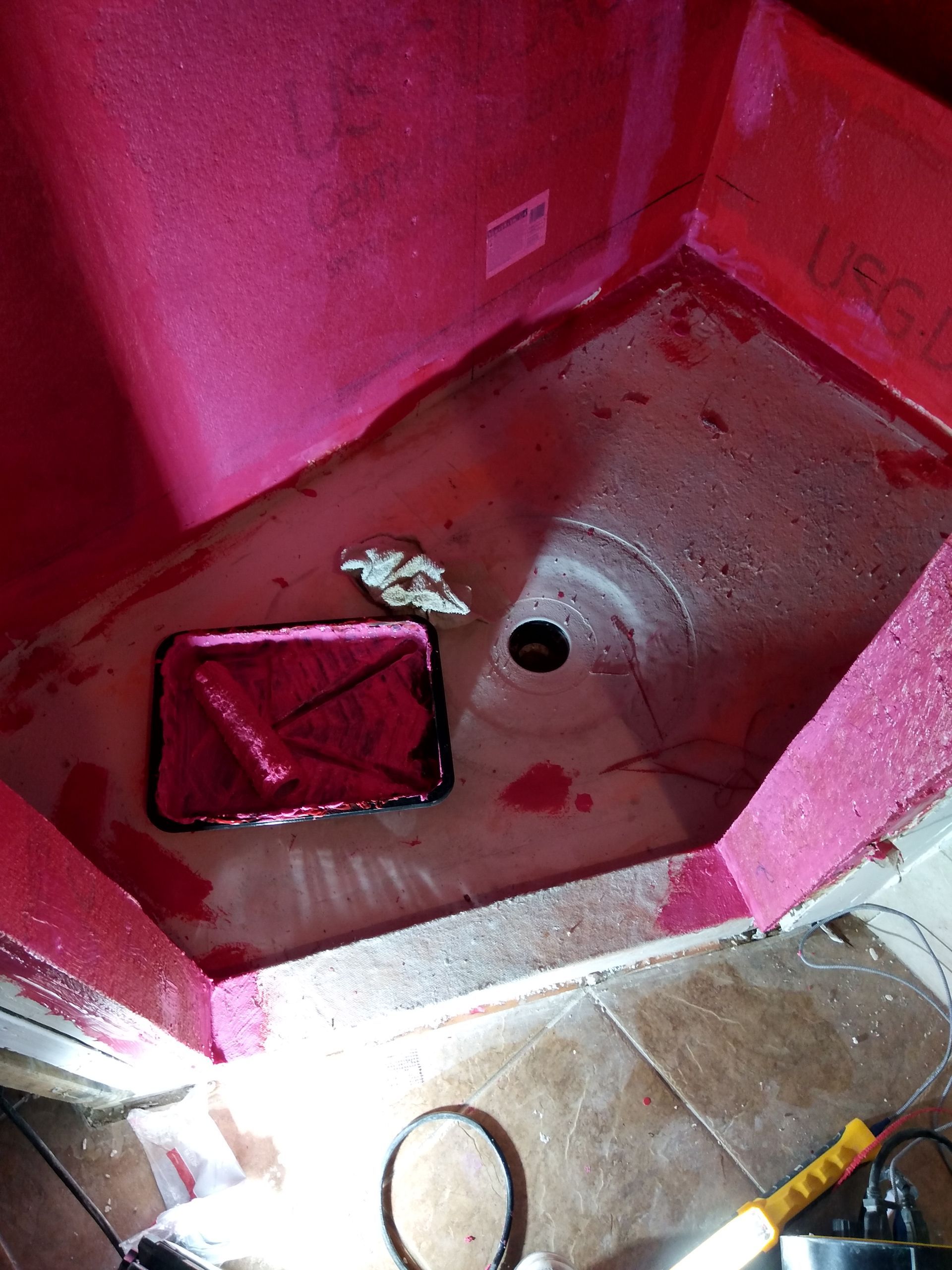 Pink shower stall with wet floor, drain, and a small towel or rag near the corner