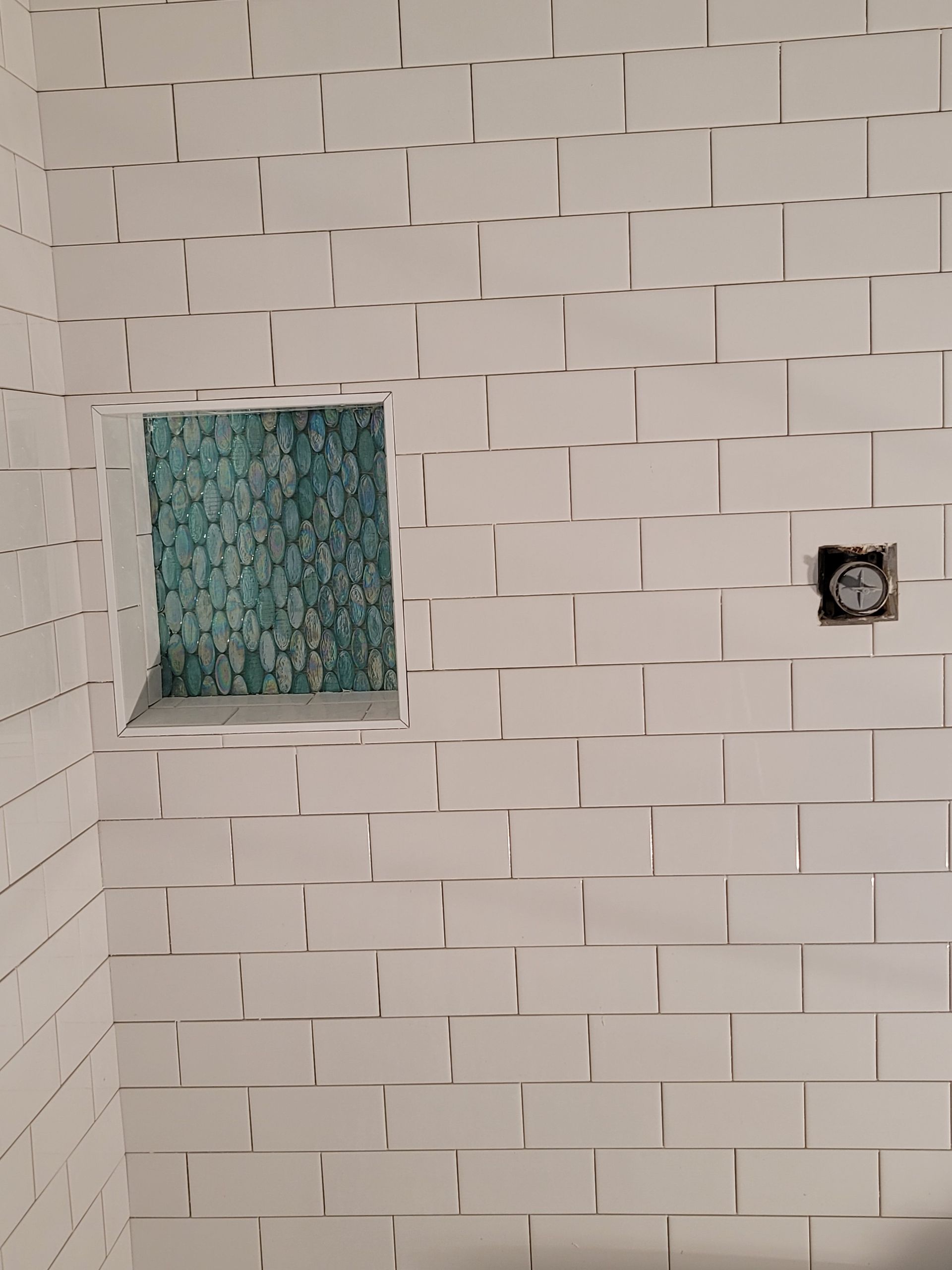 White tiled shower wall with a small recessed niche and a plumbing outlet on the right