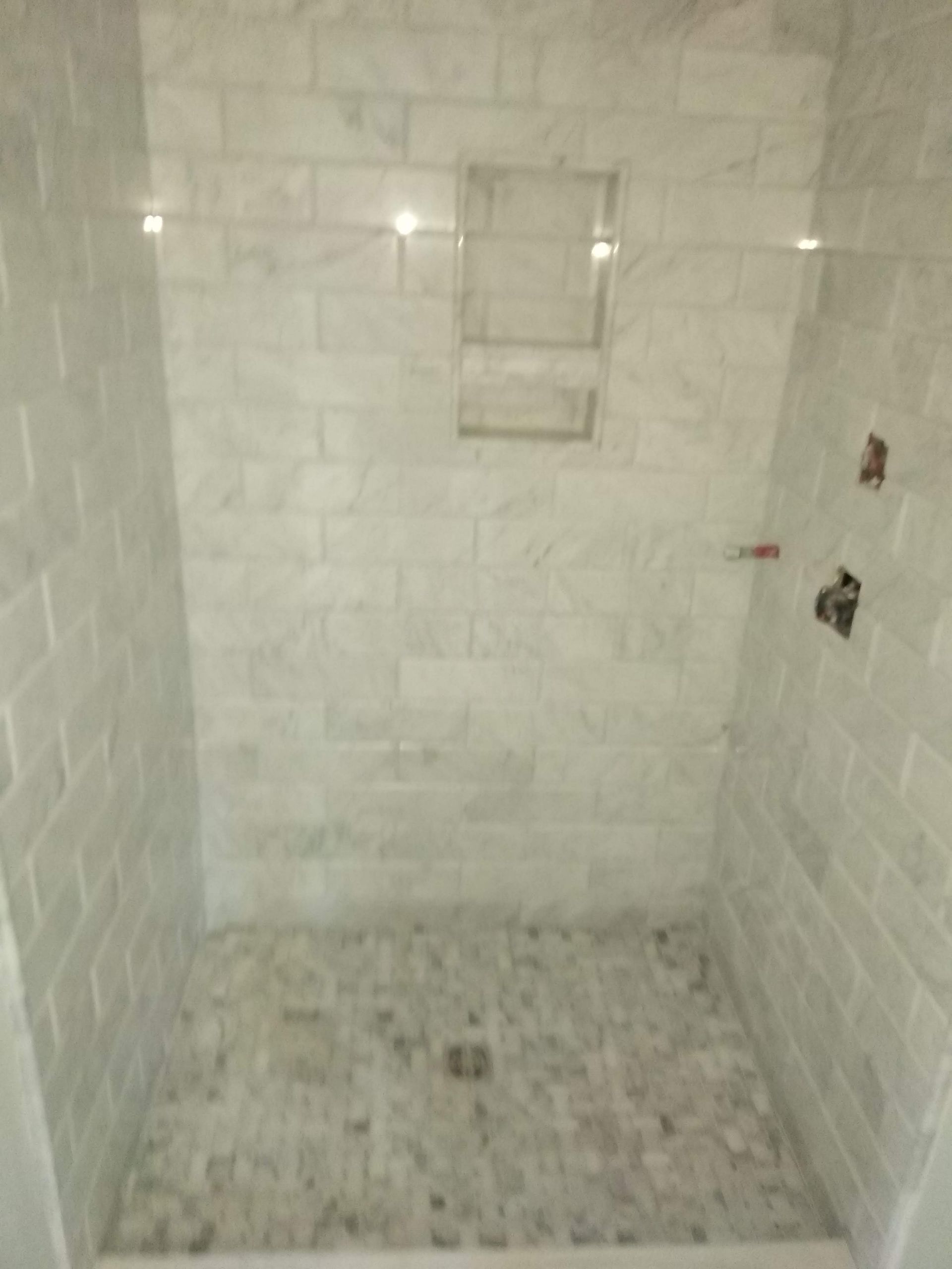 Empty tiled shower stall with small built-in shelf and mosaic floor.