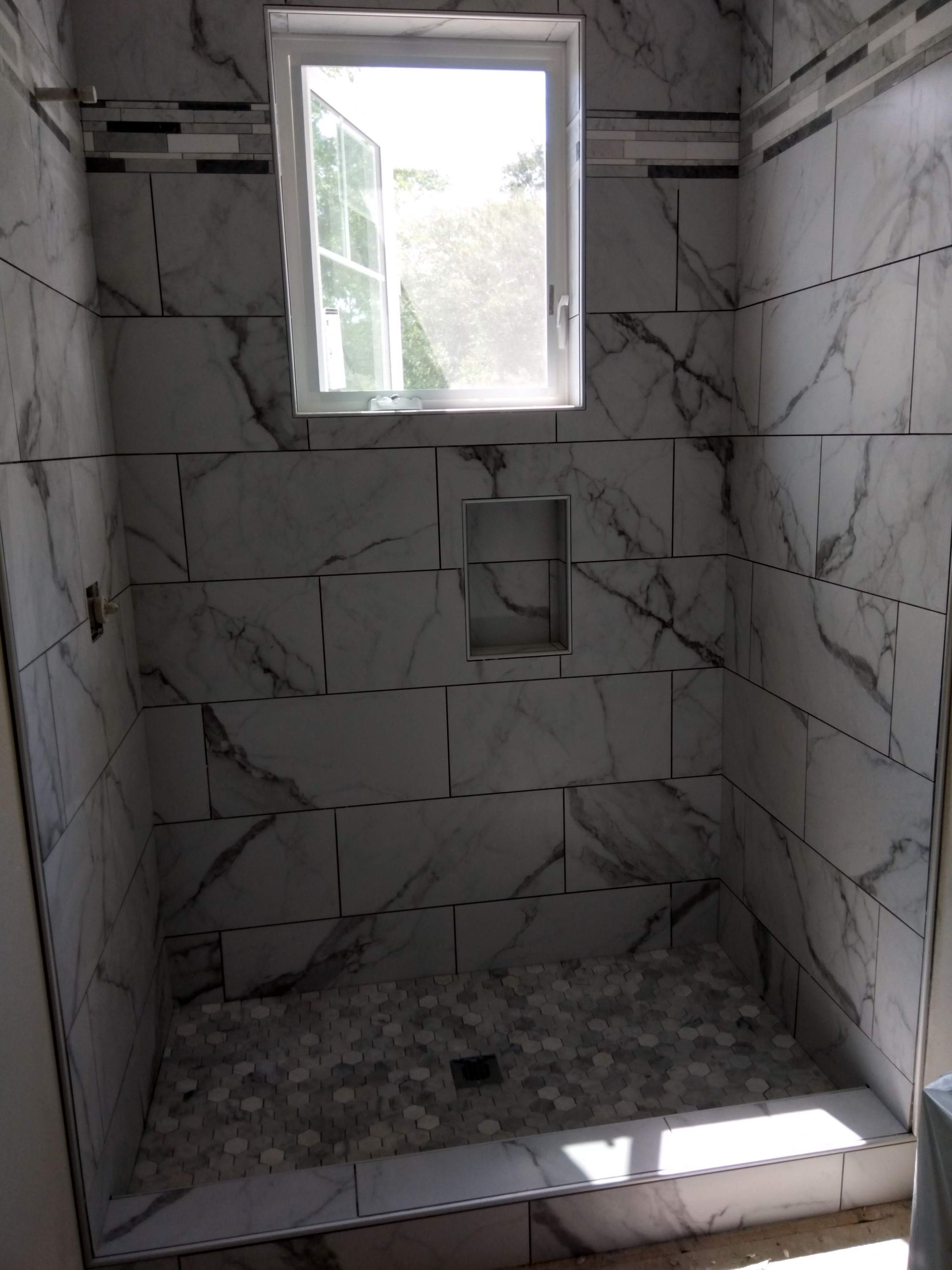 Tiled shower stall with a small window and a built-in soap niche.