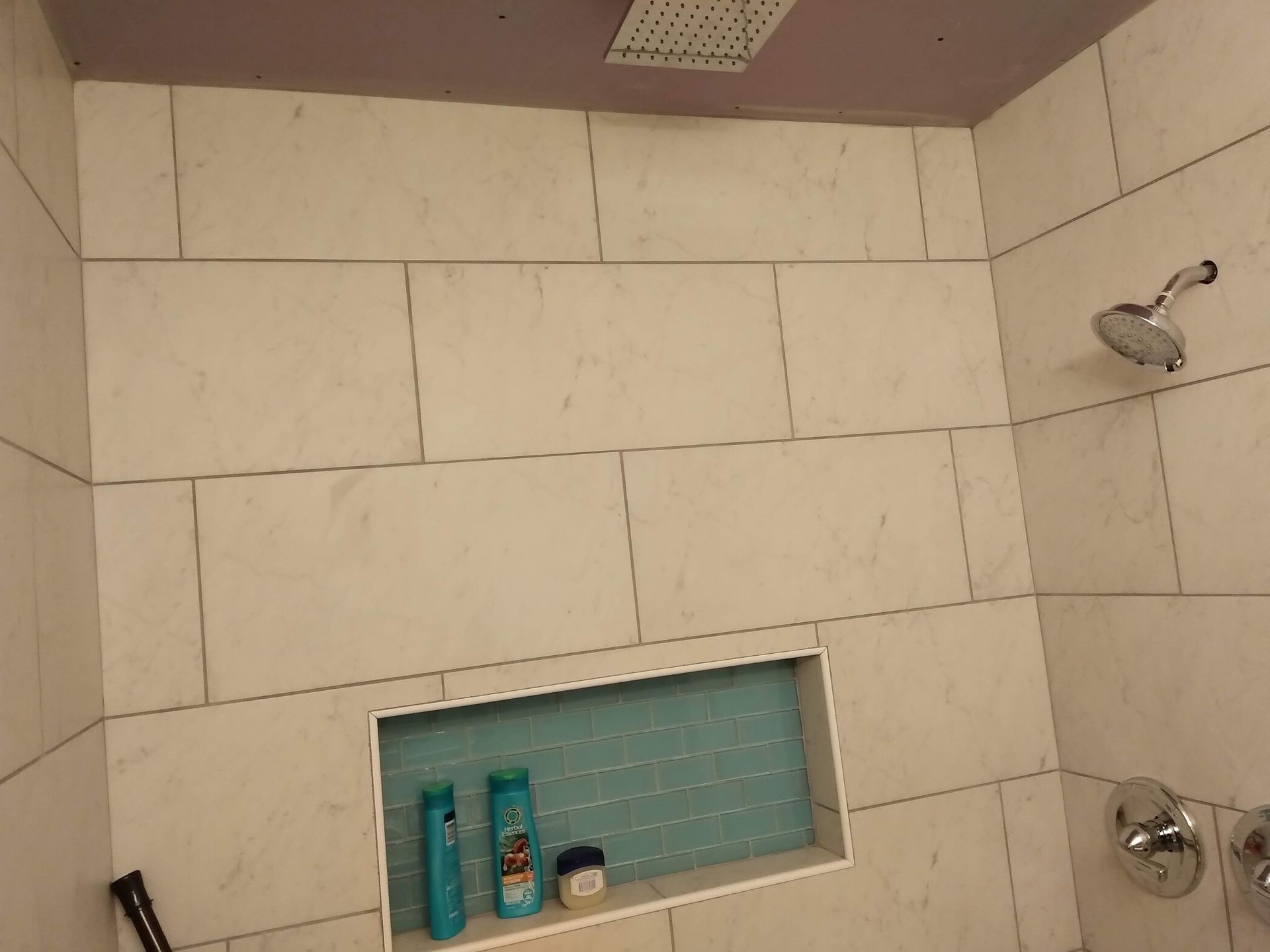 Small tiled shower with built-in shelf and chrome fixtures, viewed from inside.