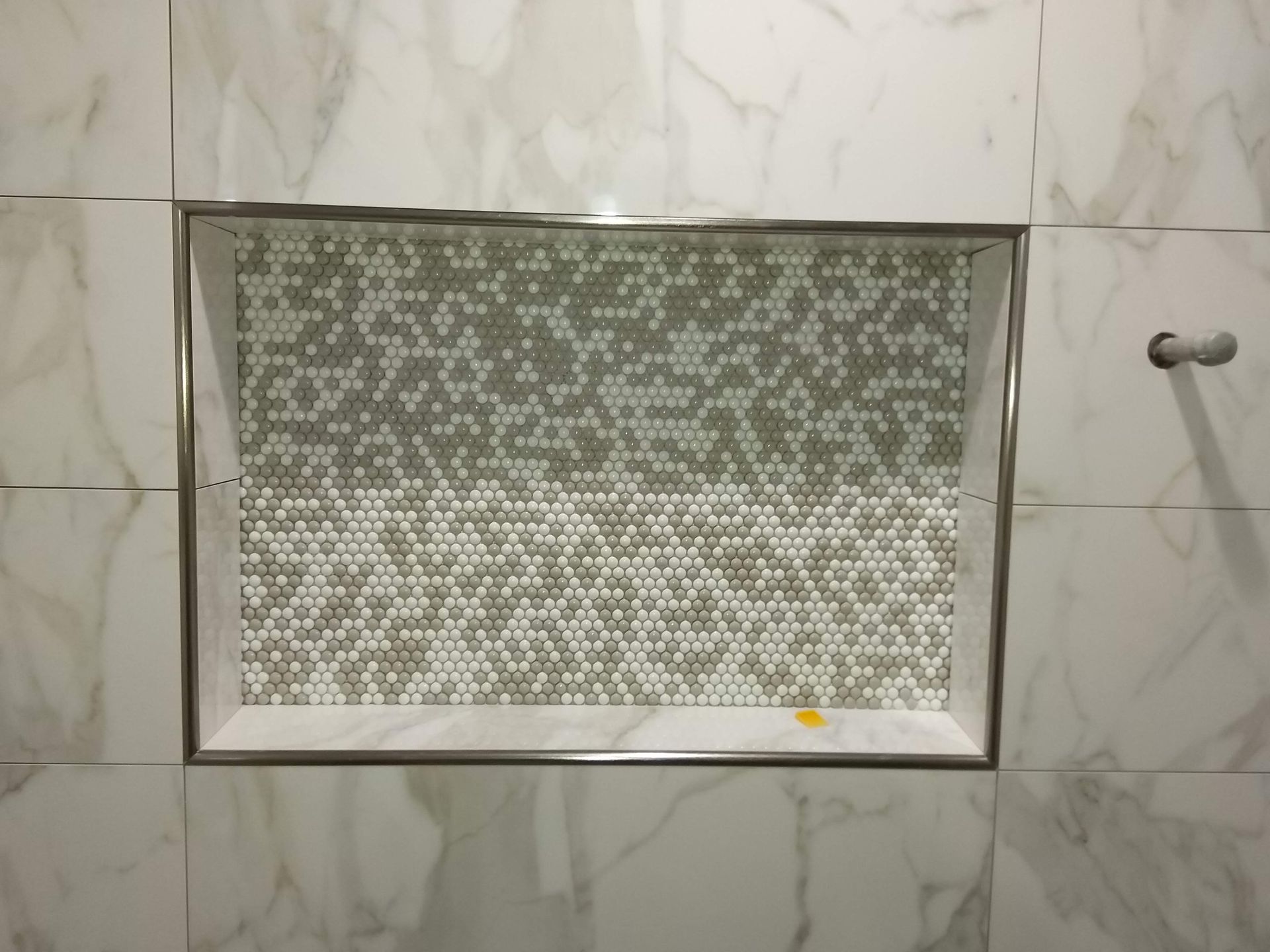 Tiled bathroom wall with a small frosted glass window and a metal handle on the right.