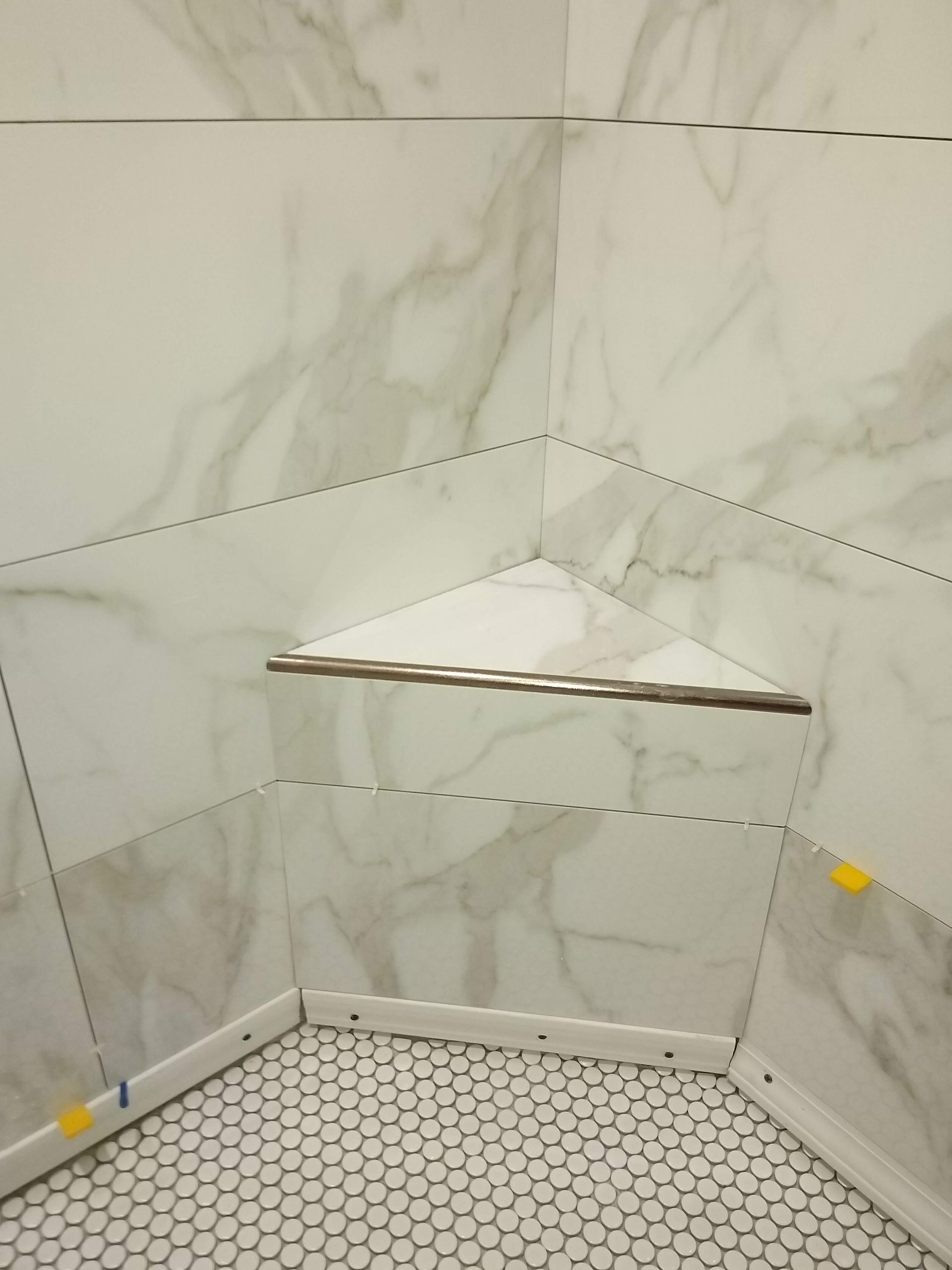 Corner shower with white marble tile, hexagon floor, and built-in corner shelf.