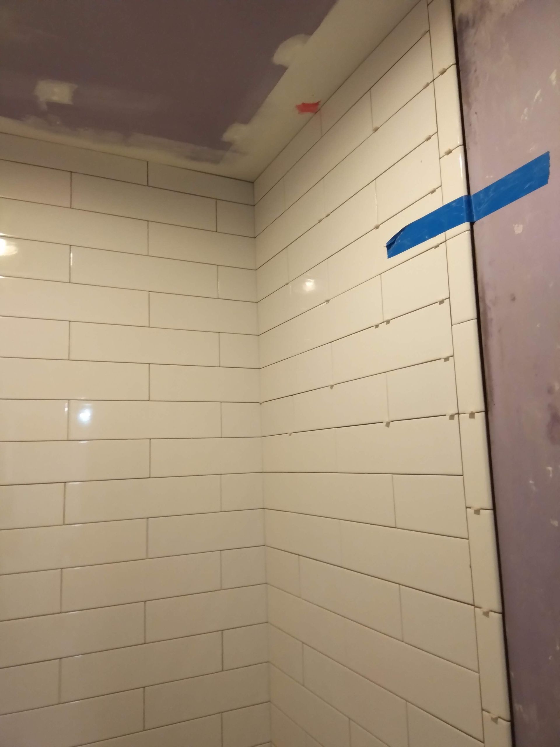 Tiled bathroom corner with unfinished ceiling, dark purple wall, and blue painter’s tape on the right wall