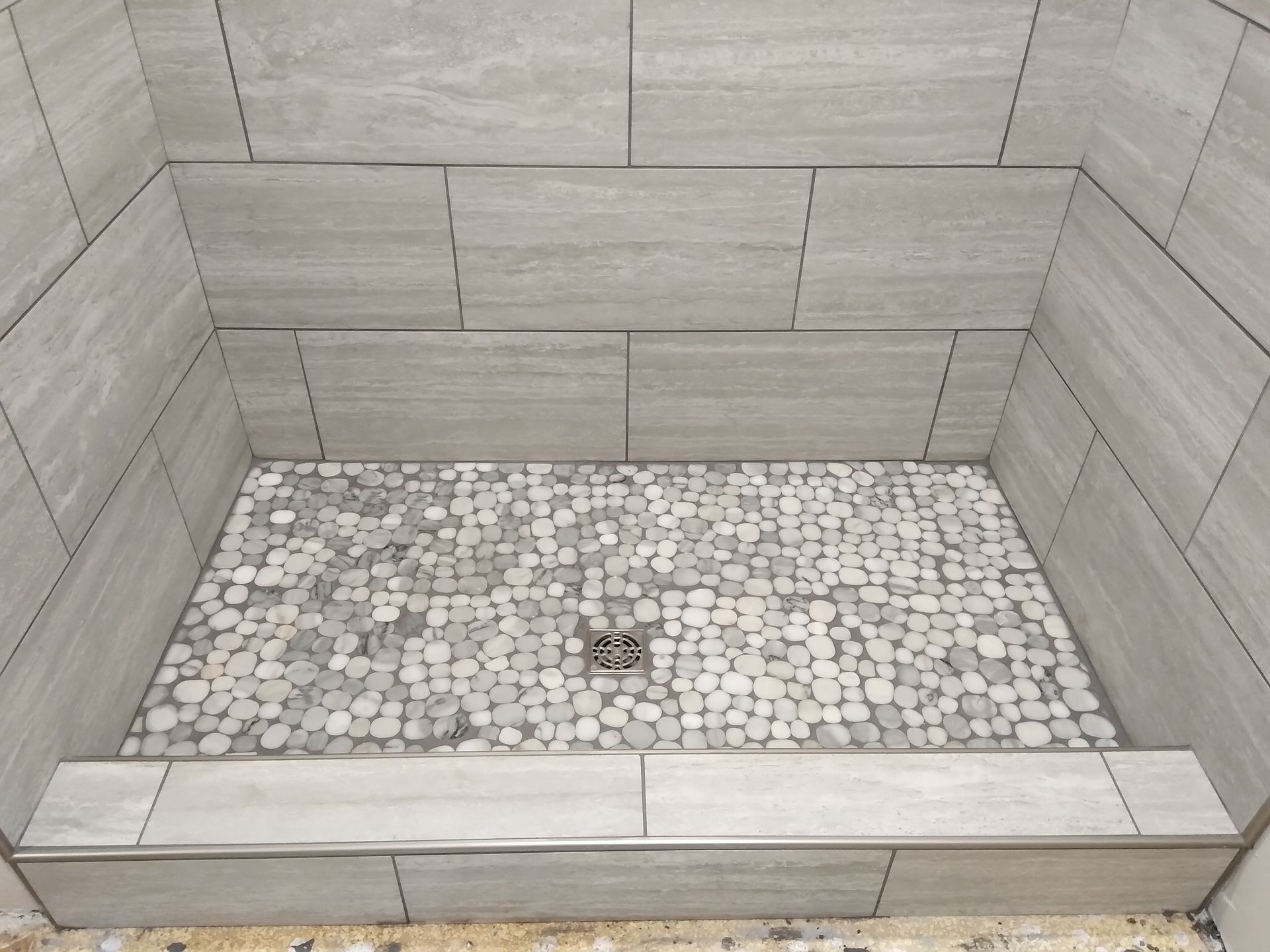 Empty tiled shower with pebble floor and bench seat