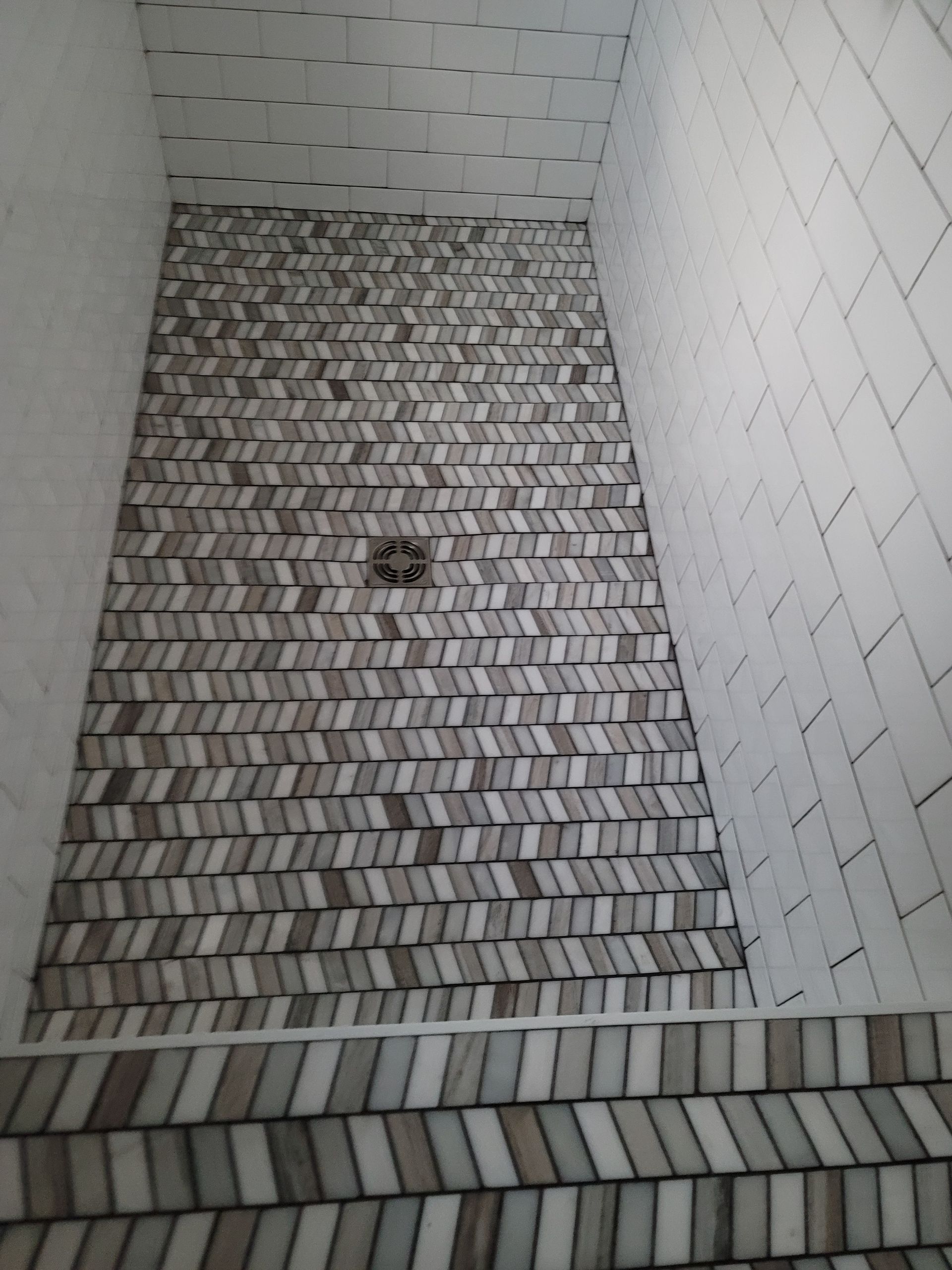 Empty tiled shower floor with a drain in the center and white tiled walls.