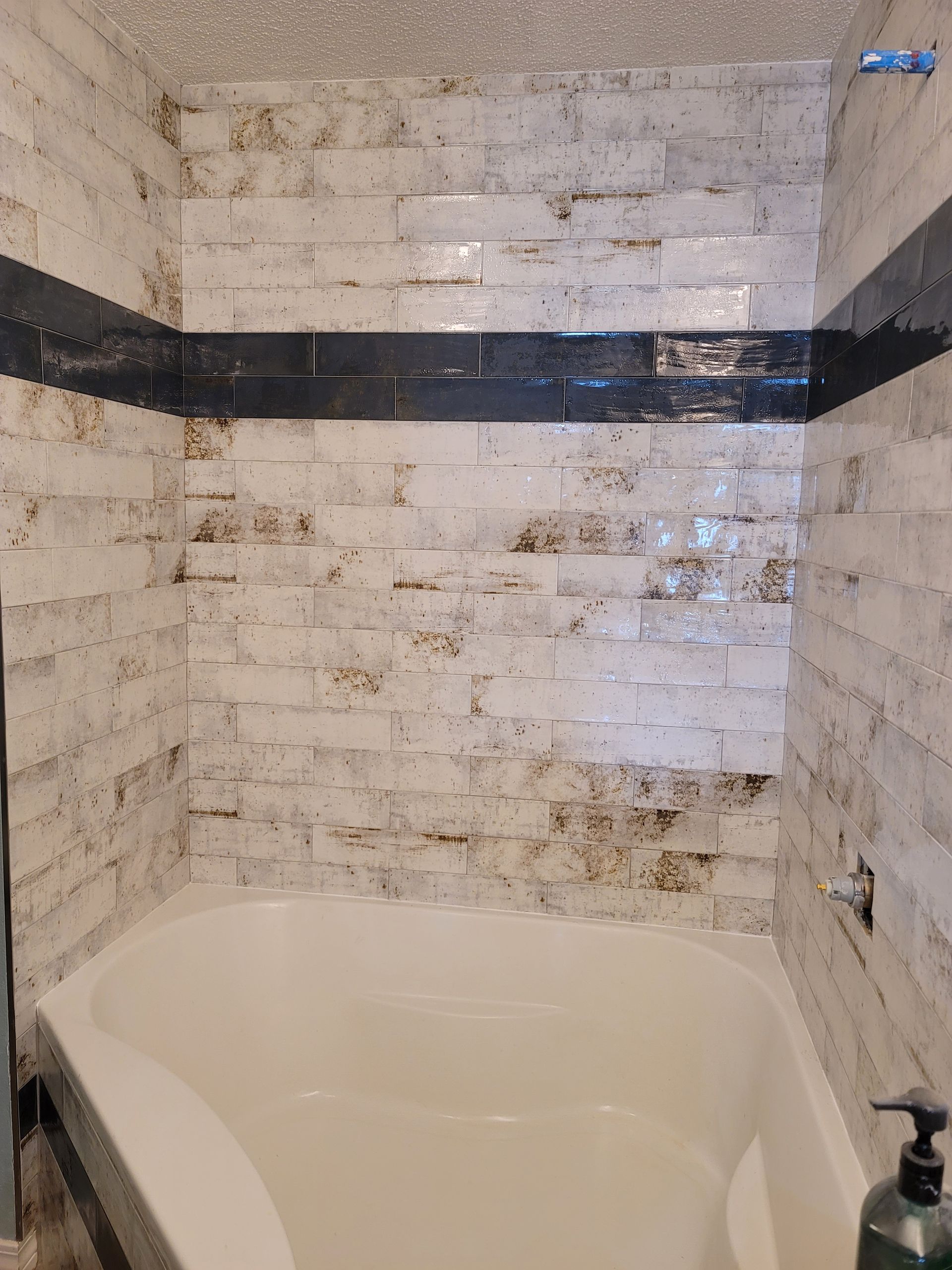 White tiled bathroom with a black accent stripe and a bathtub/shower alcove