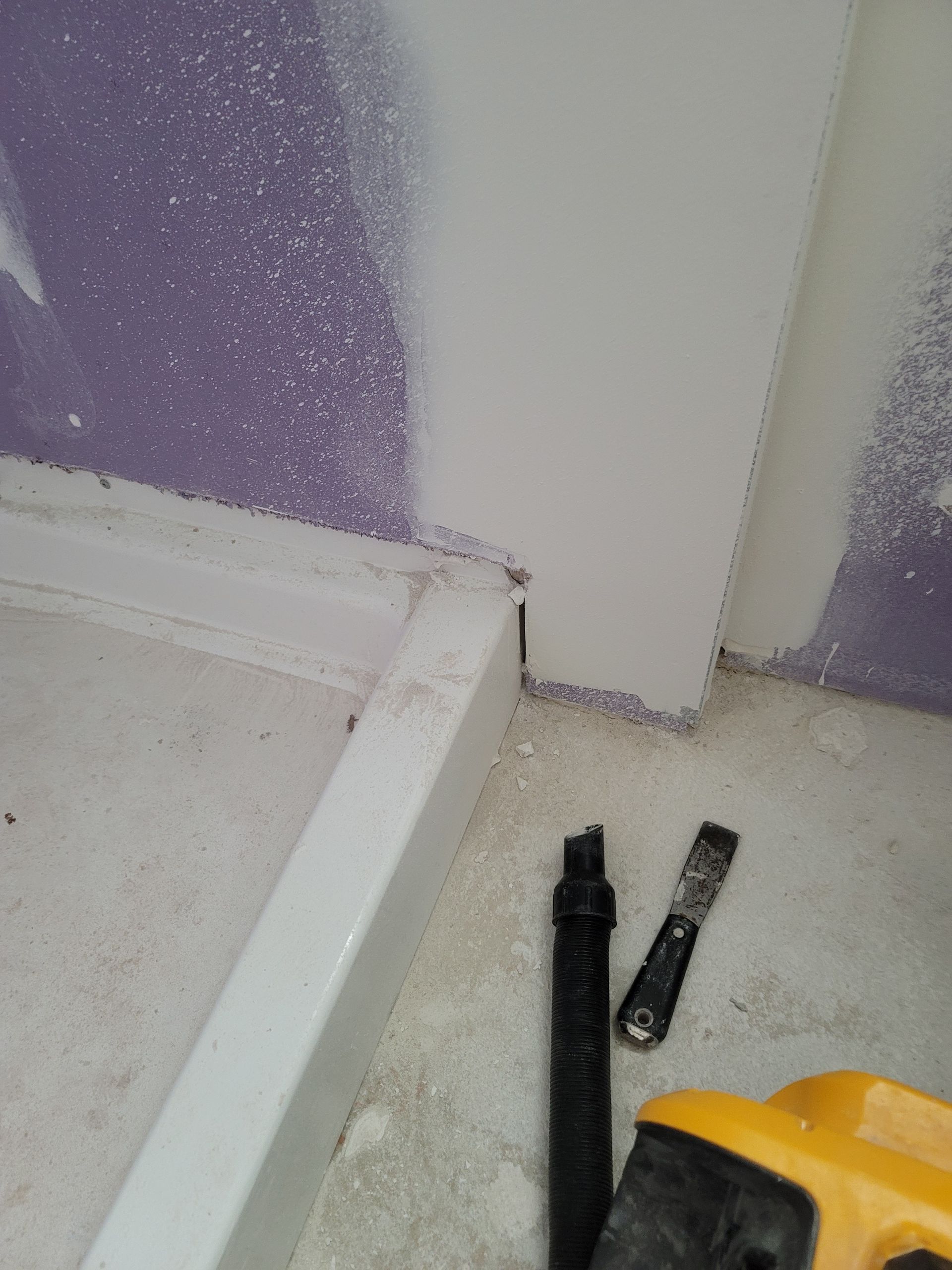 White cabinet beside purple wall with black trim pieces on a dusty floor and a yellow tool case
