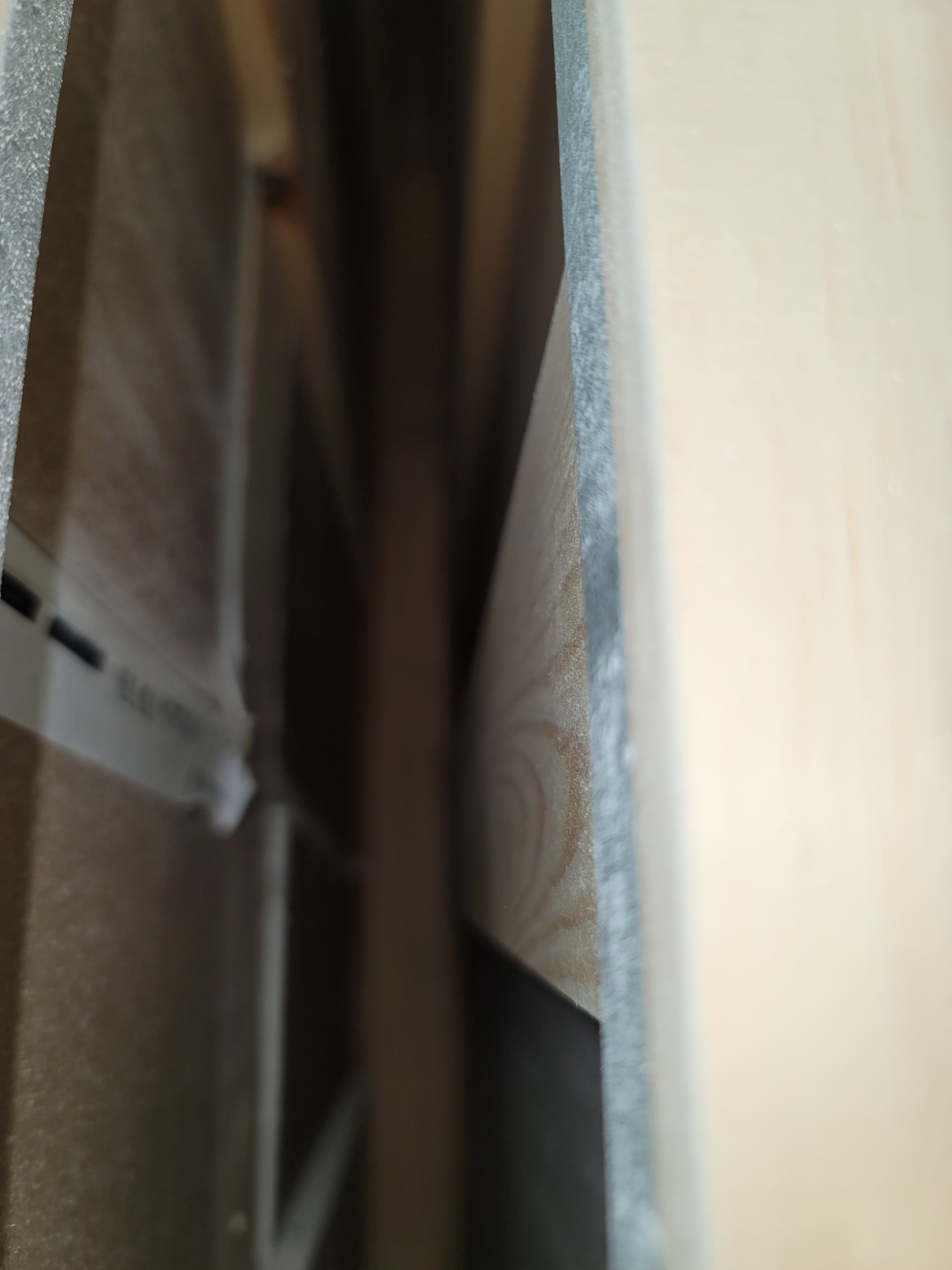 Close-up of a narrow gap between a dark wooden panel and a light wall, showing patterned fabric.