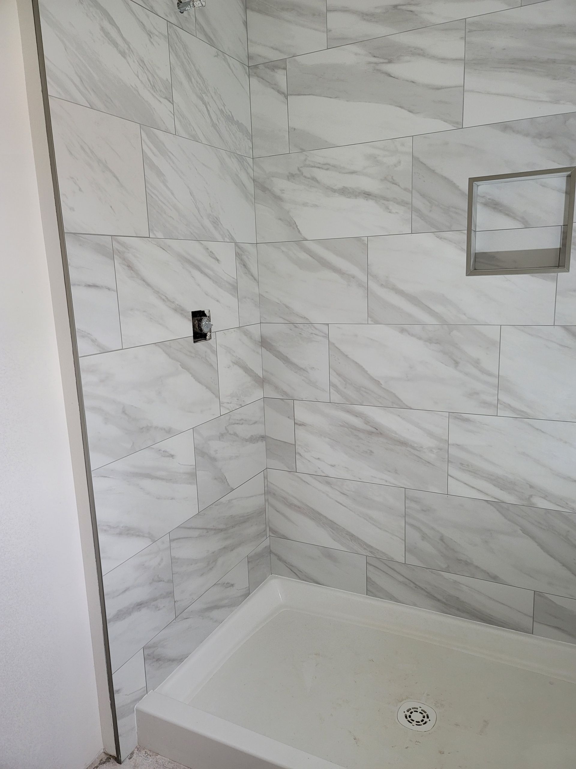 Empty tiled shower corner with a built-in bench and wall fixture hole