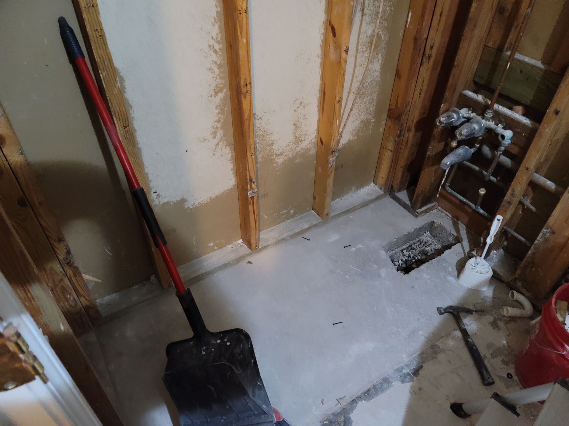 Renovation area with exposed wall studs, a shovel, and plumbing pipes in a small room